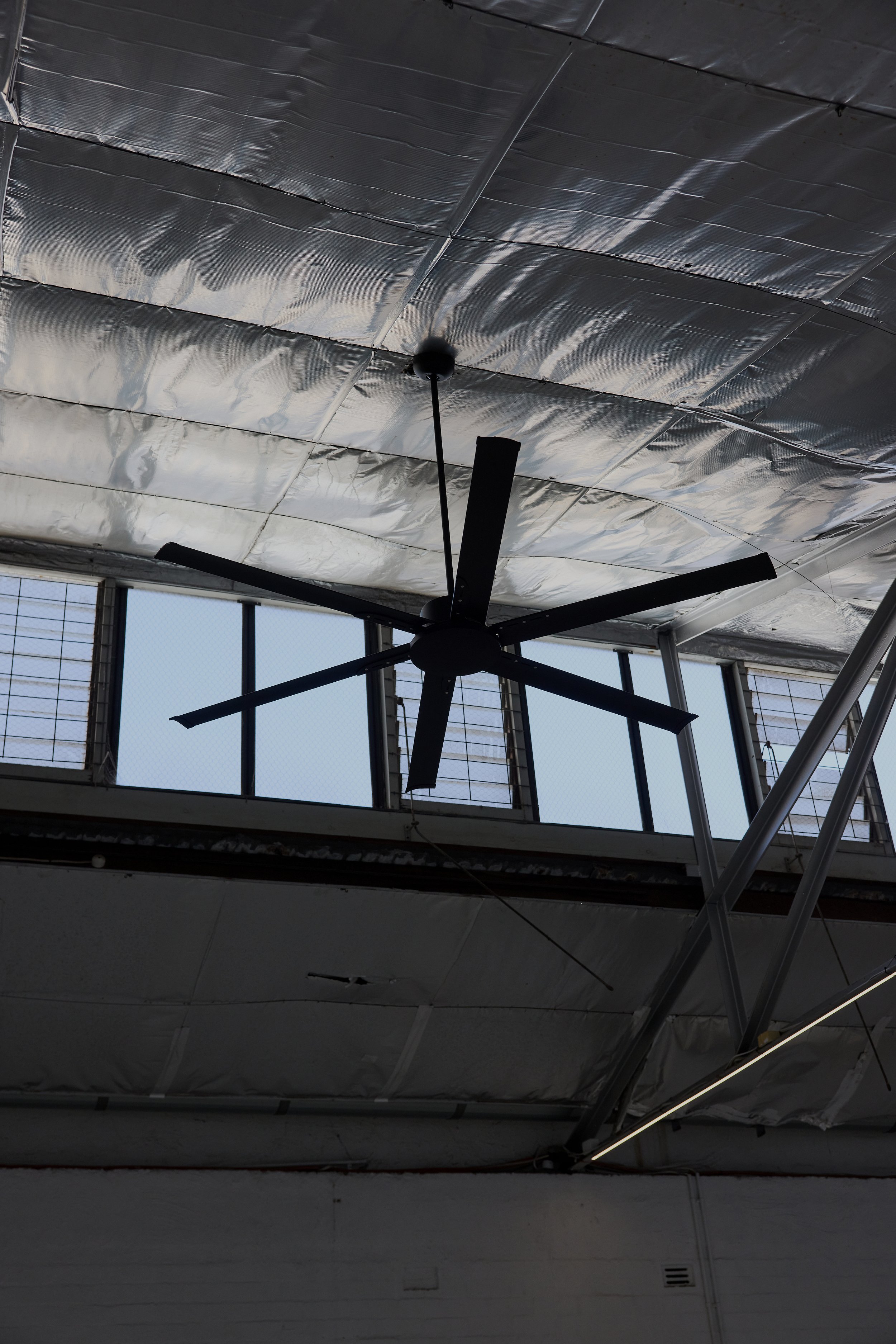 Ceiling with a black ceiling fan, industrial-style windows with metal bars, and silver insulation panels on the ceiling.