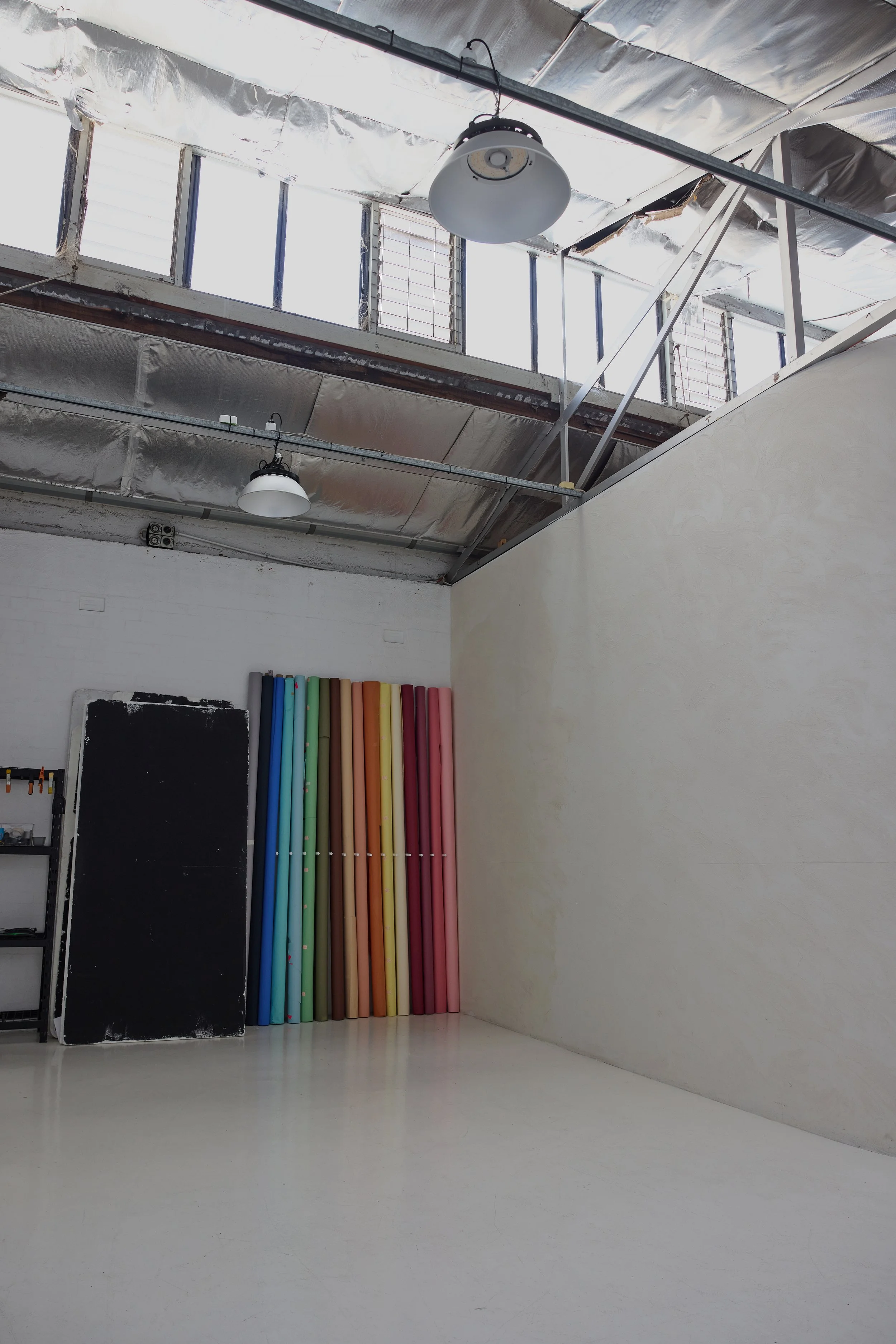 Interior of a studio or creative space with colorful foam rollers, a blackboard, and shelves with supplies. The ceiling has industrial lighting and exposed ductwork.