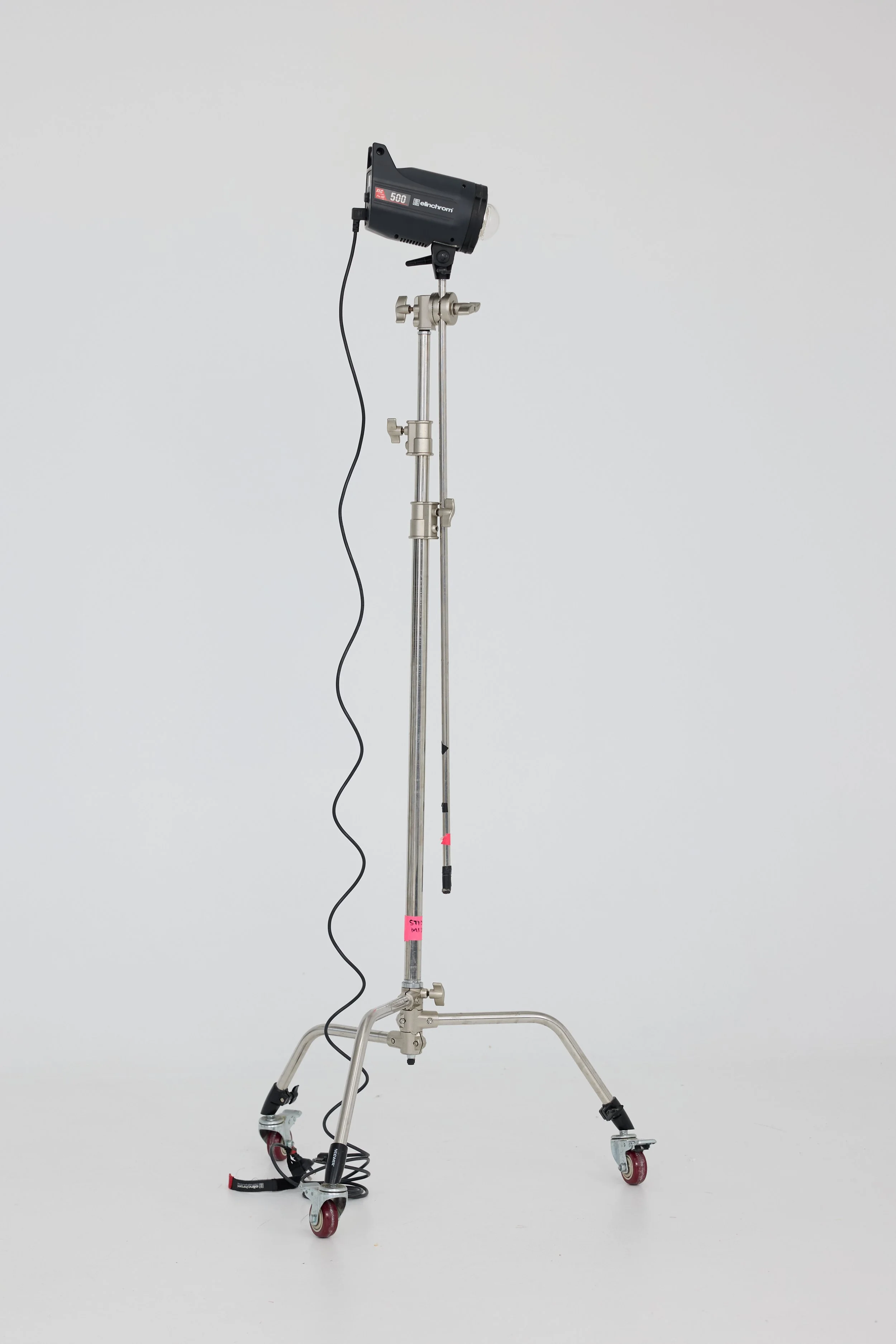 A professional studio light on a mobile stand with wheels, connected to a power cord, set against a plain white background.