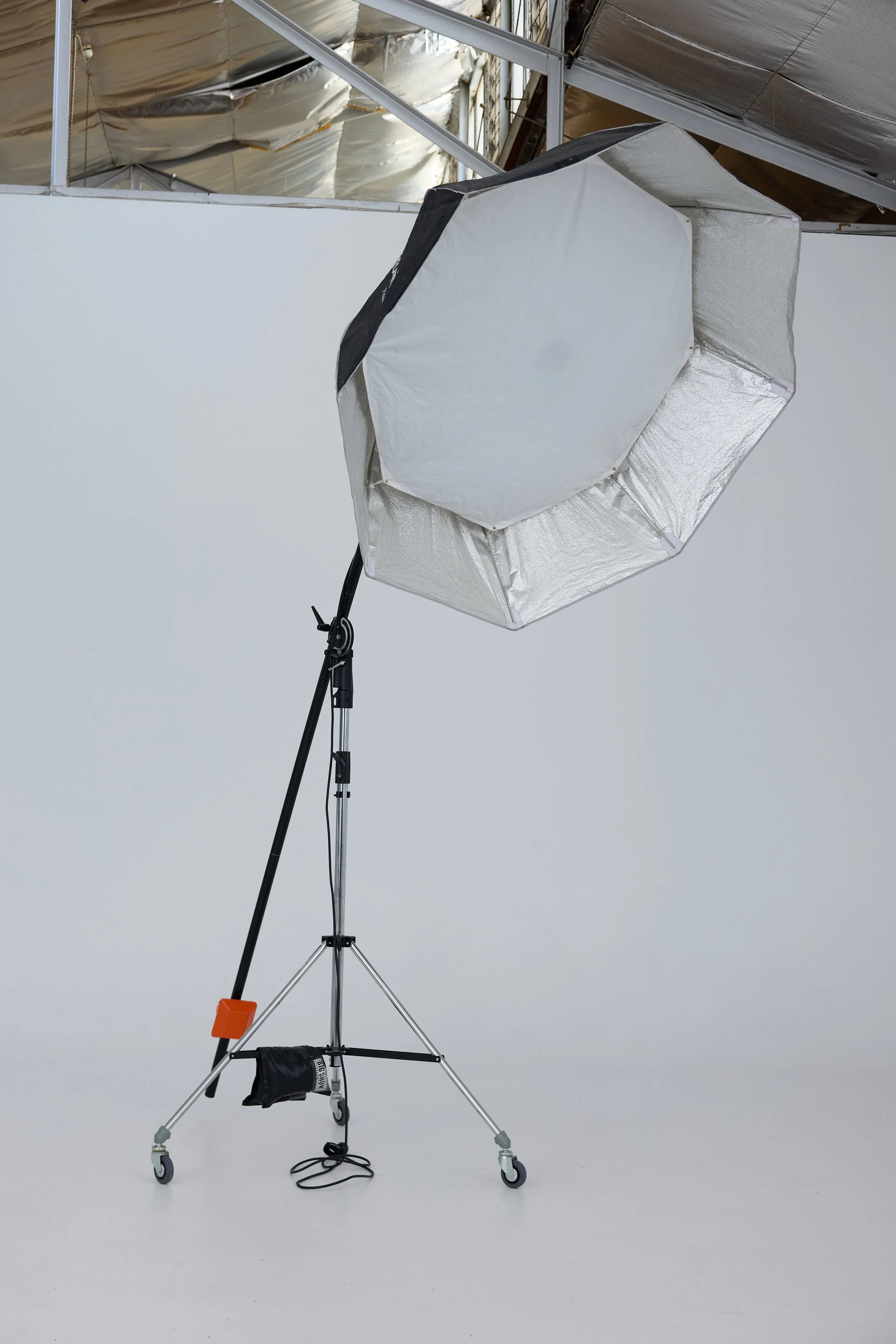 Photography studio softbox light with reflective interior, on adjustable stand with wheels, against a plain white background.