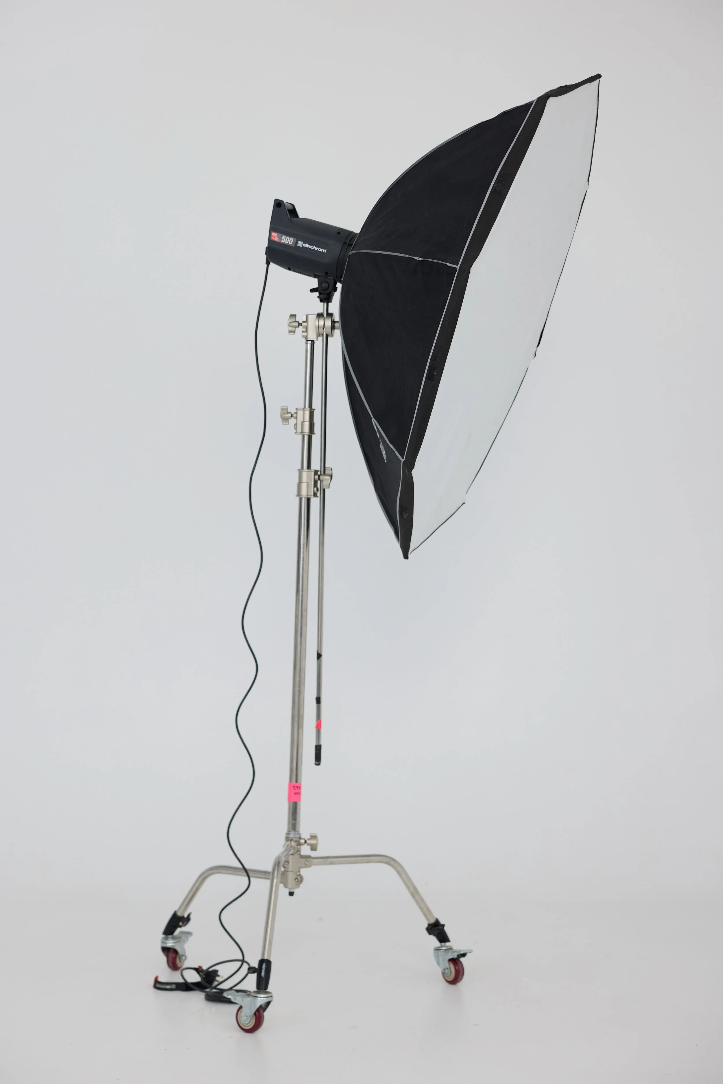 Studio lighting equipment with a large umbrella reflector on a stand with wheels.