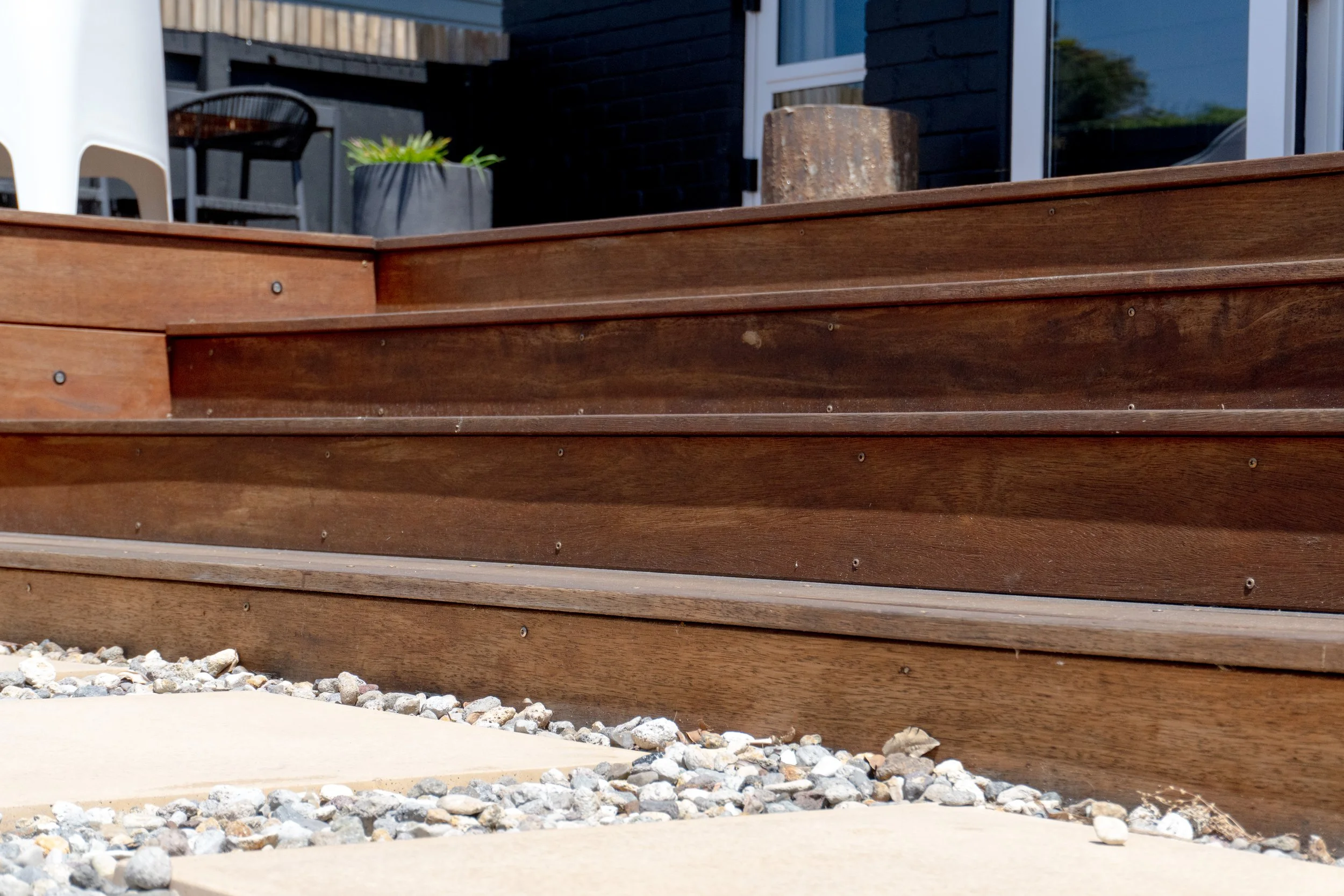 Close-up of wooden steps leading up to a house patio with gravel and concrete in the foreground.