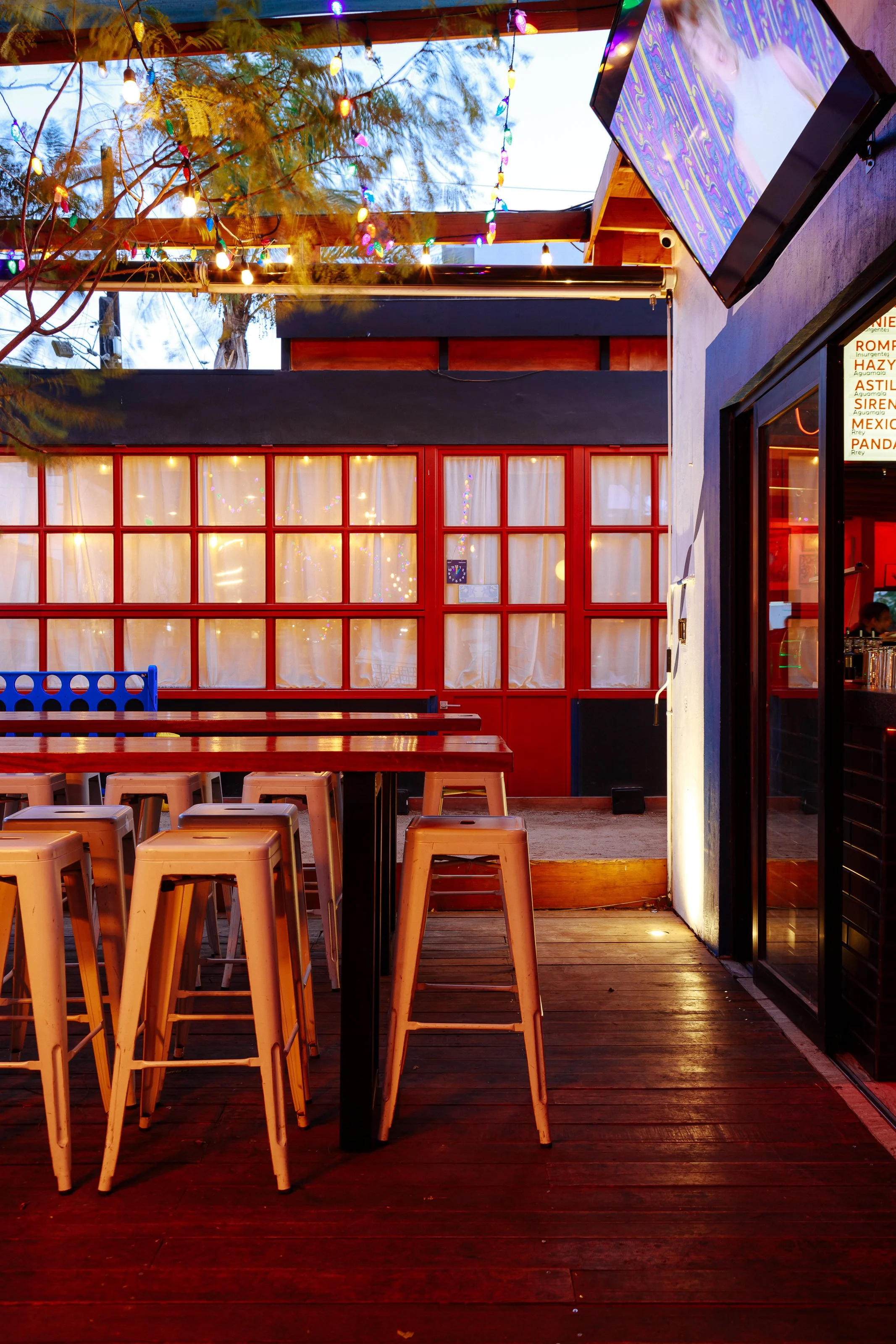 Outdoor patio with high tables, stools, string lights, and TV screen