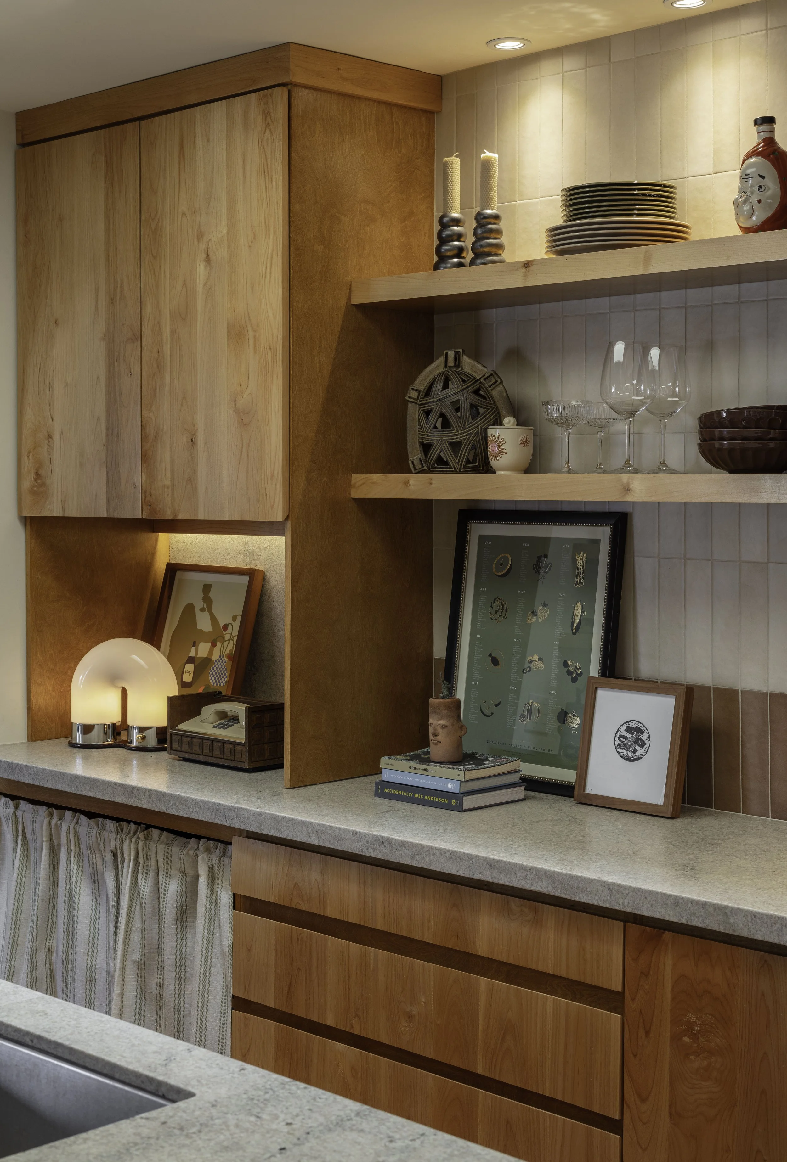 Wooden kitchen shelves and cabinets with decorative items, plates, glasses, artwork, and books.