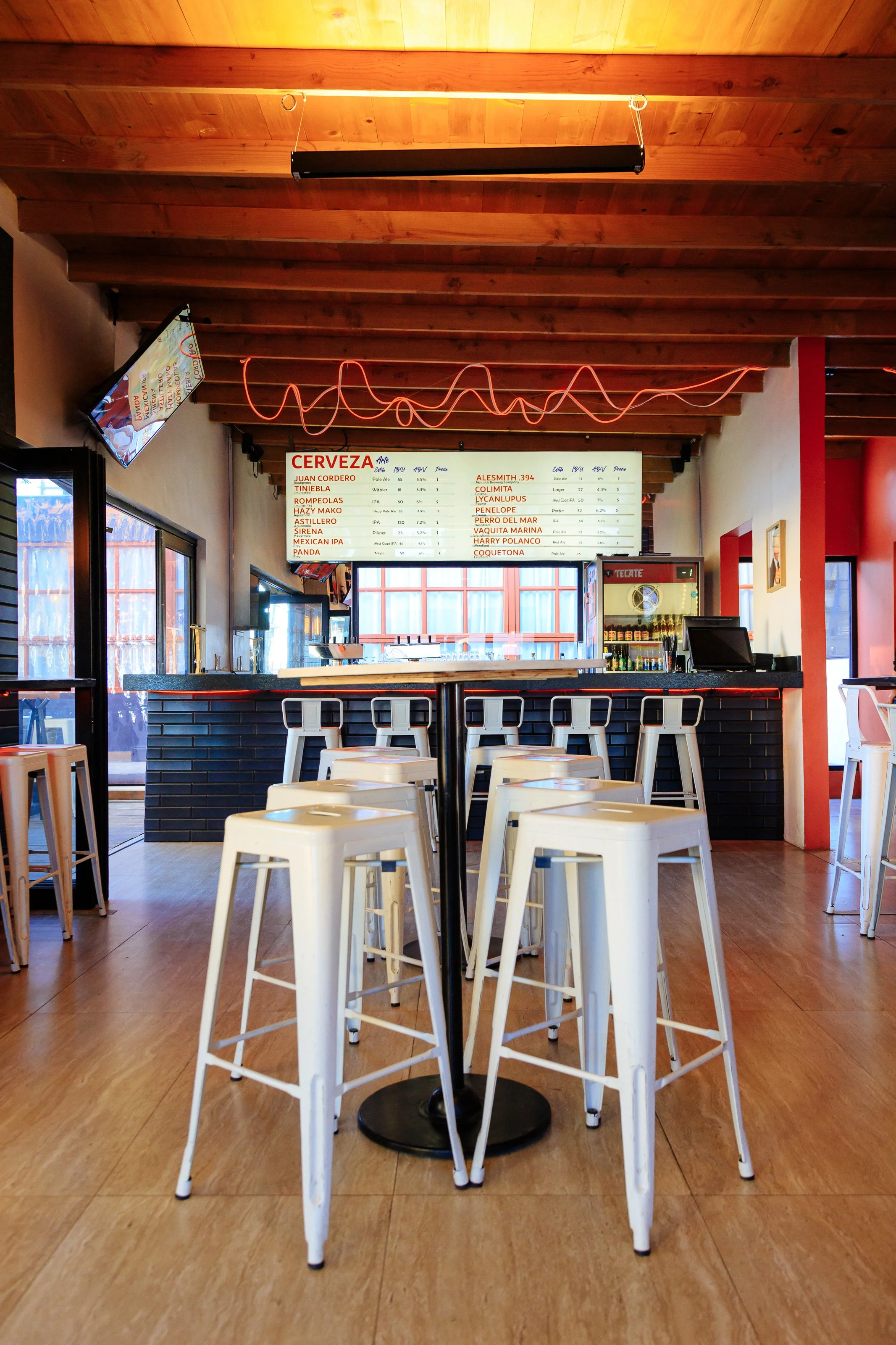 Interior of a modern bar with white metal stools, wooden ceiling, and menu board.