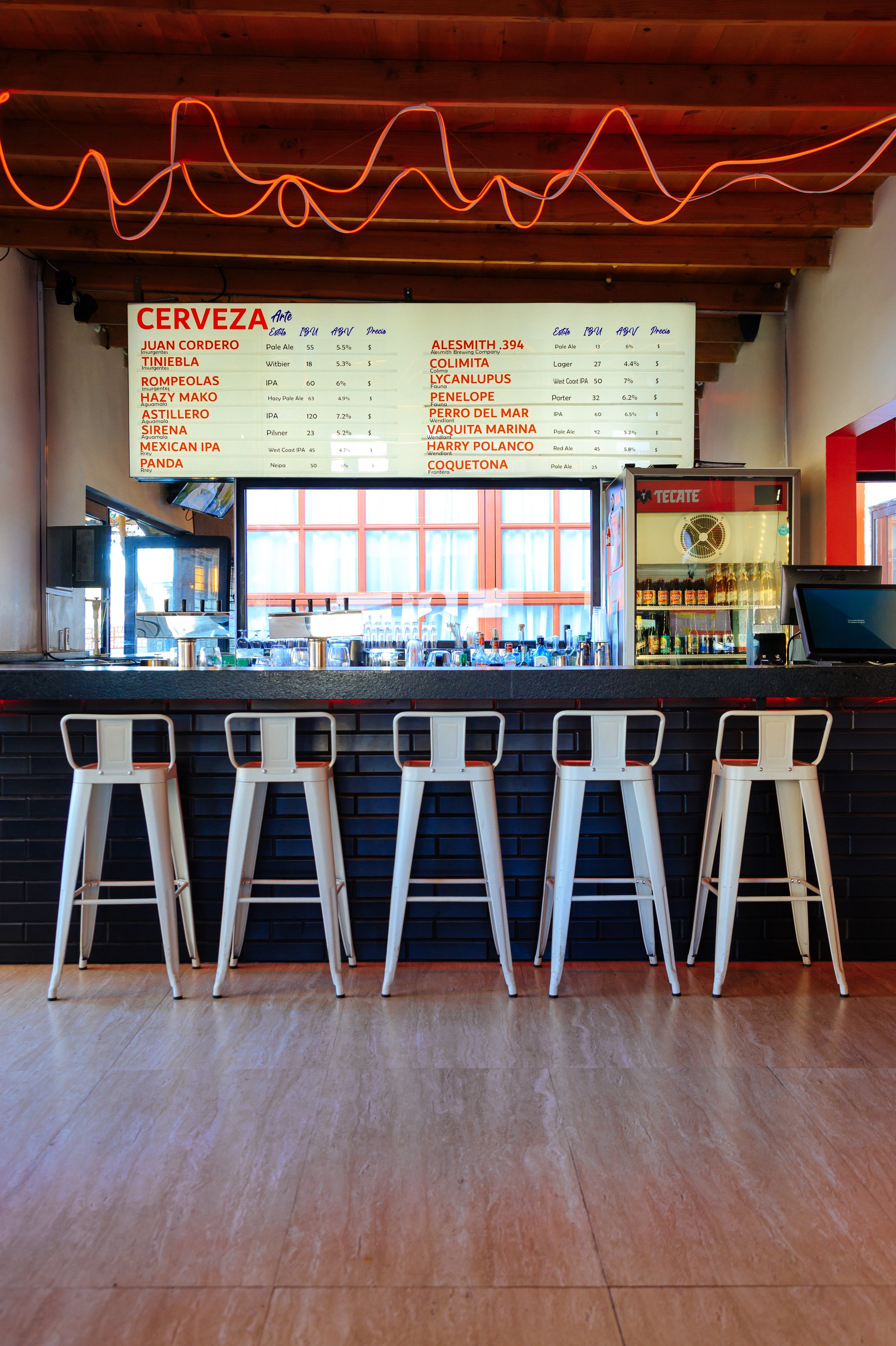 Interior of a bar with a counter, barstools, and a beer menu overhead.