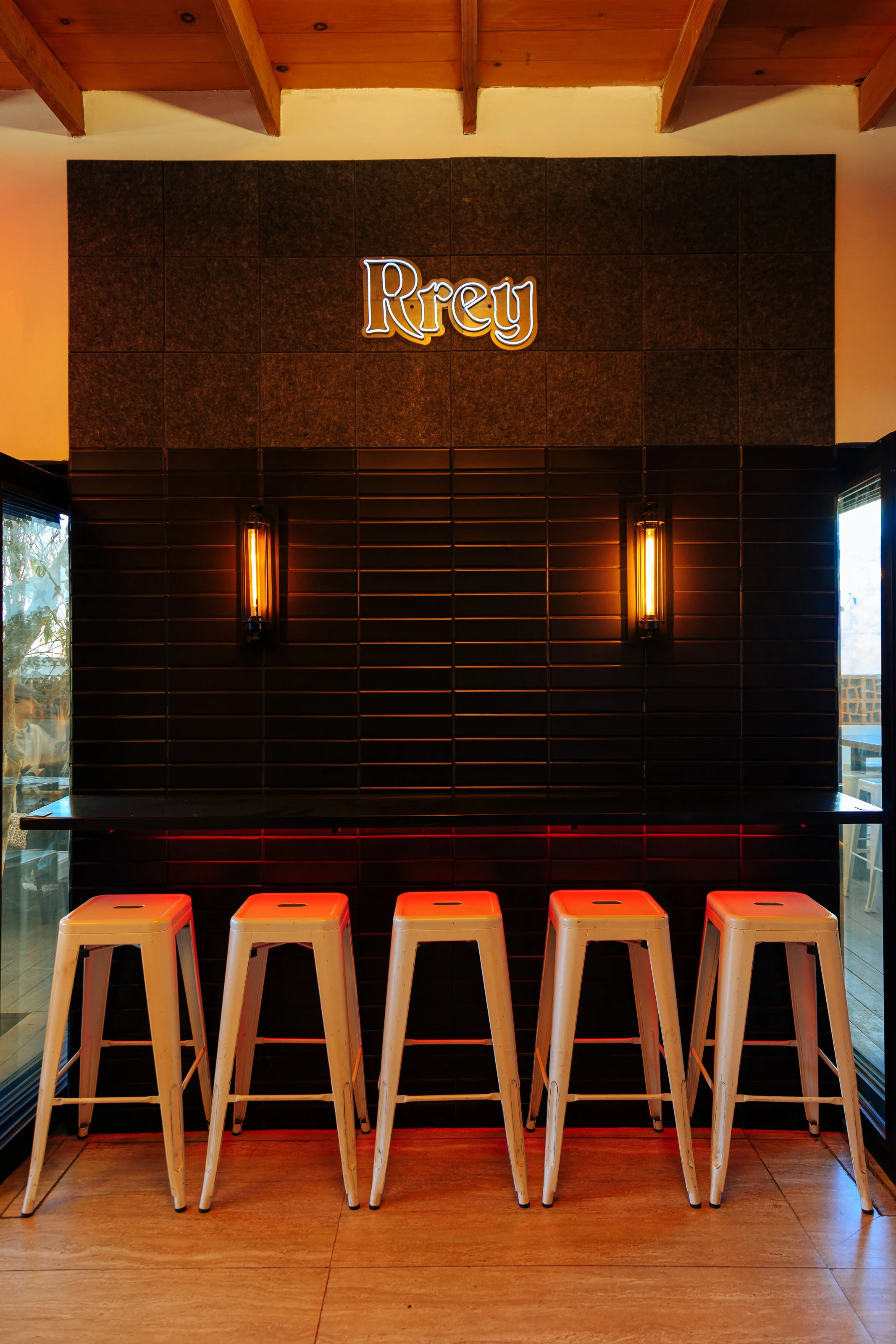 Bar area with high stools, black wall tiles, wall sconces, and a sign reading 'Rrey'.