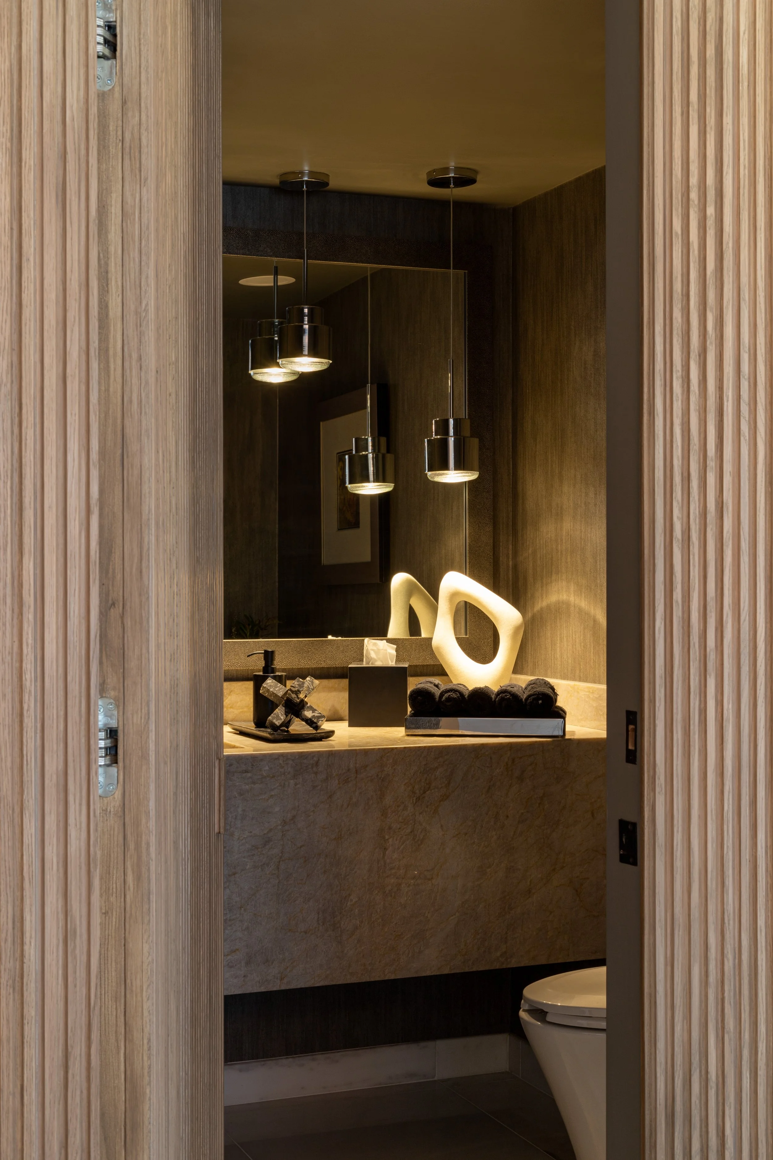 Modern bathroom with pendant lights, wooden walls, stone countertop, decorative objects, and a toilet.