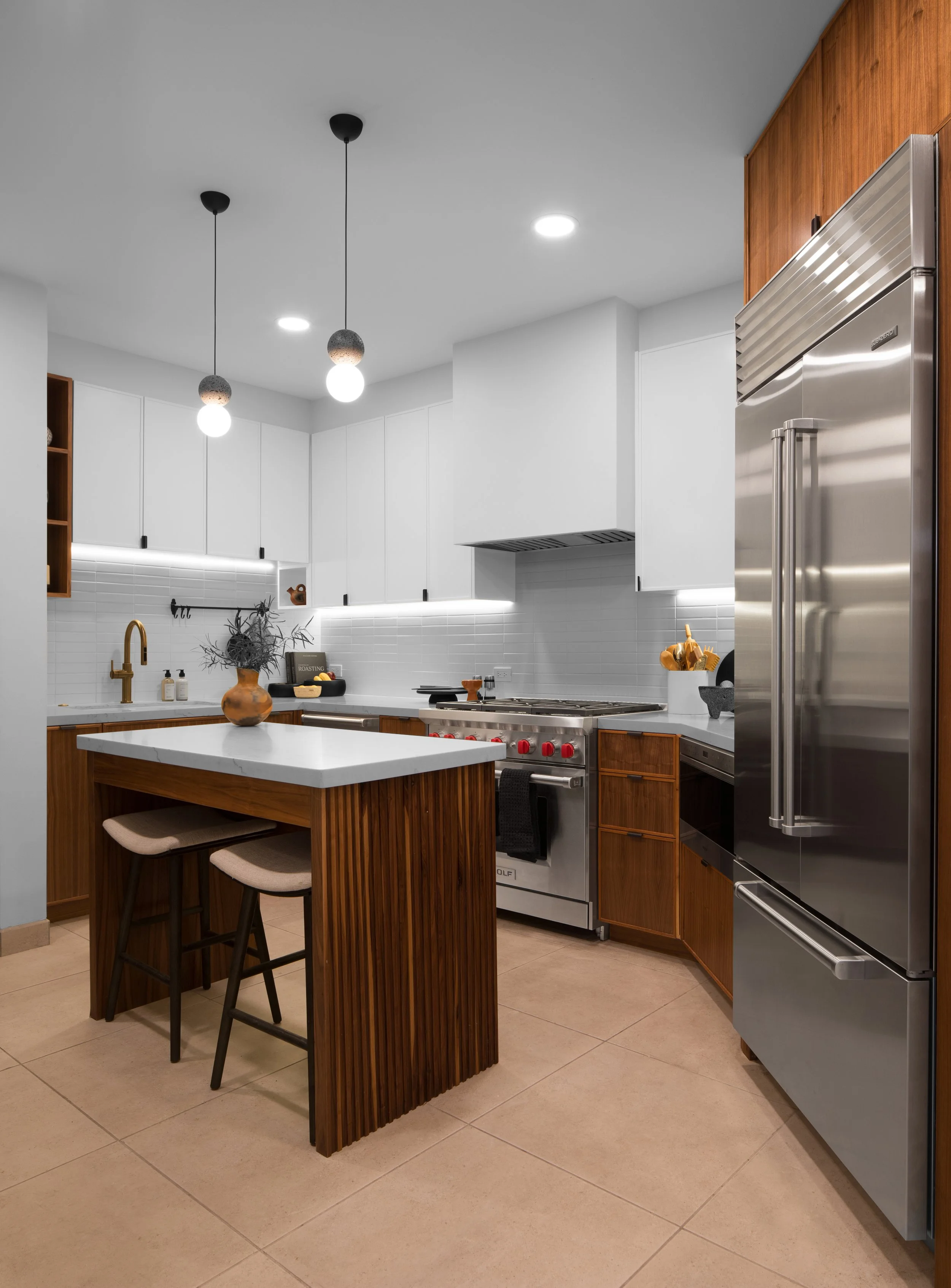 Modern kitchen with stainless steel appliances, white cabinets, wood accents, pendant lighting, and a central island with stools.