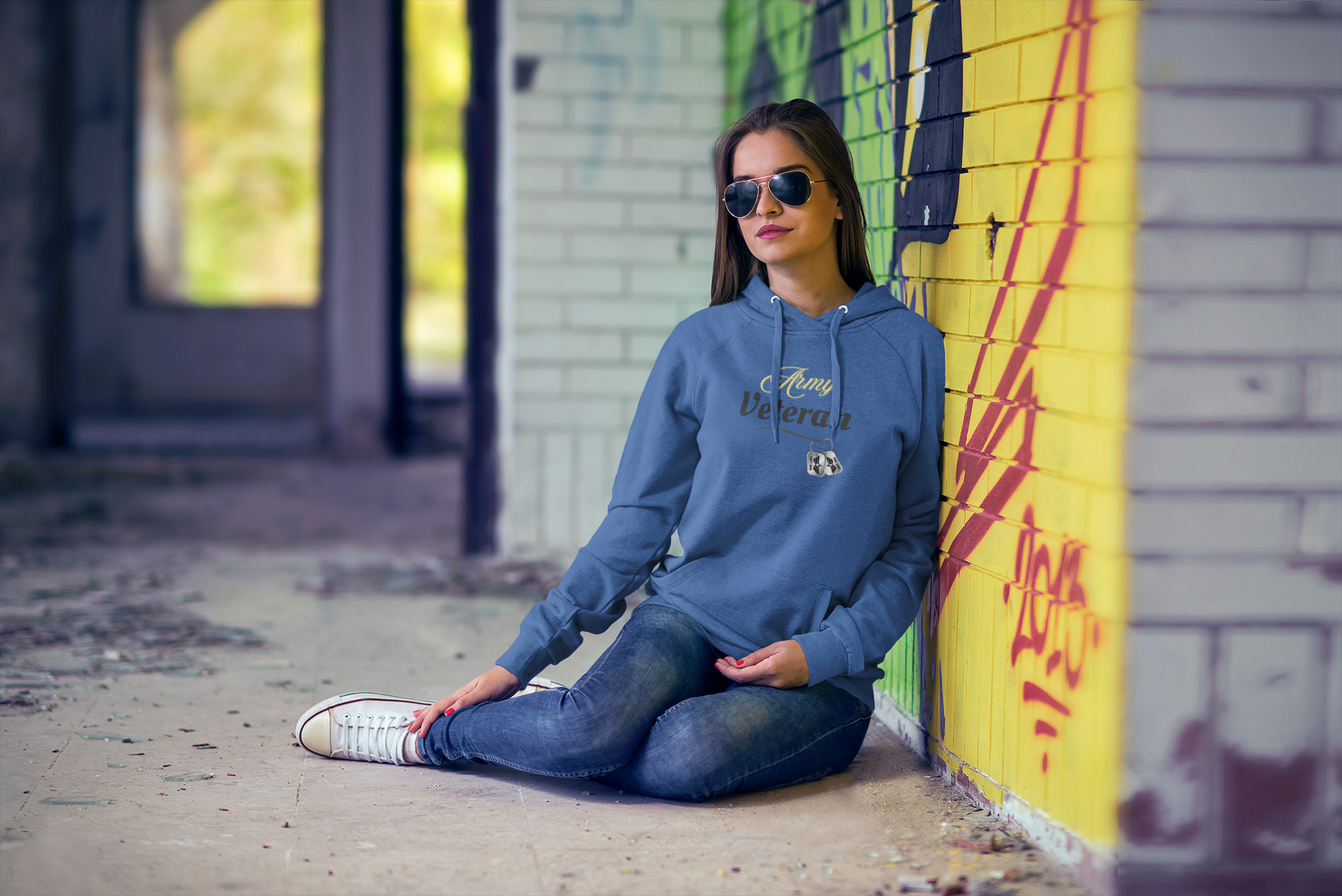 A young woman with curly hair sitting outdoors on a crosswalk, wearing a light gray hoodie with the phrase "Power Moves Only" and a crown graphic on the front.