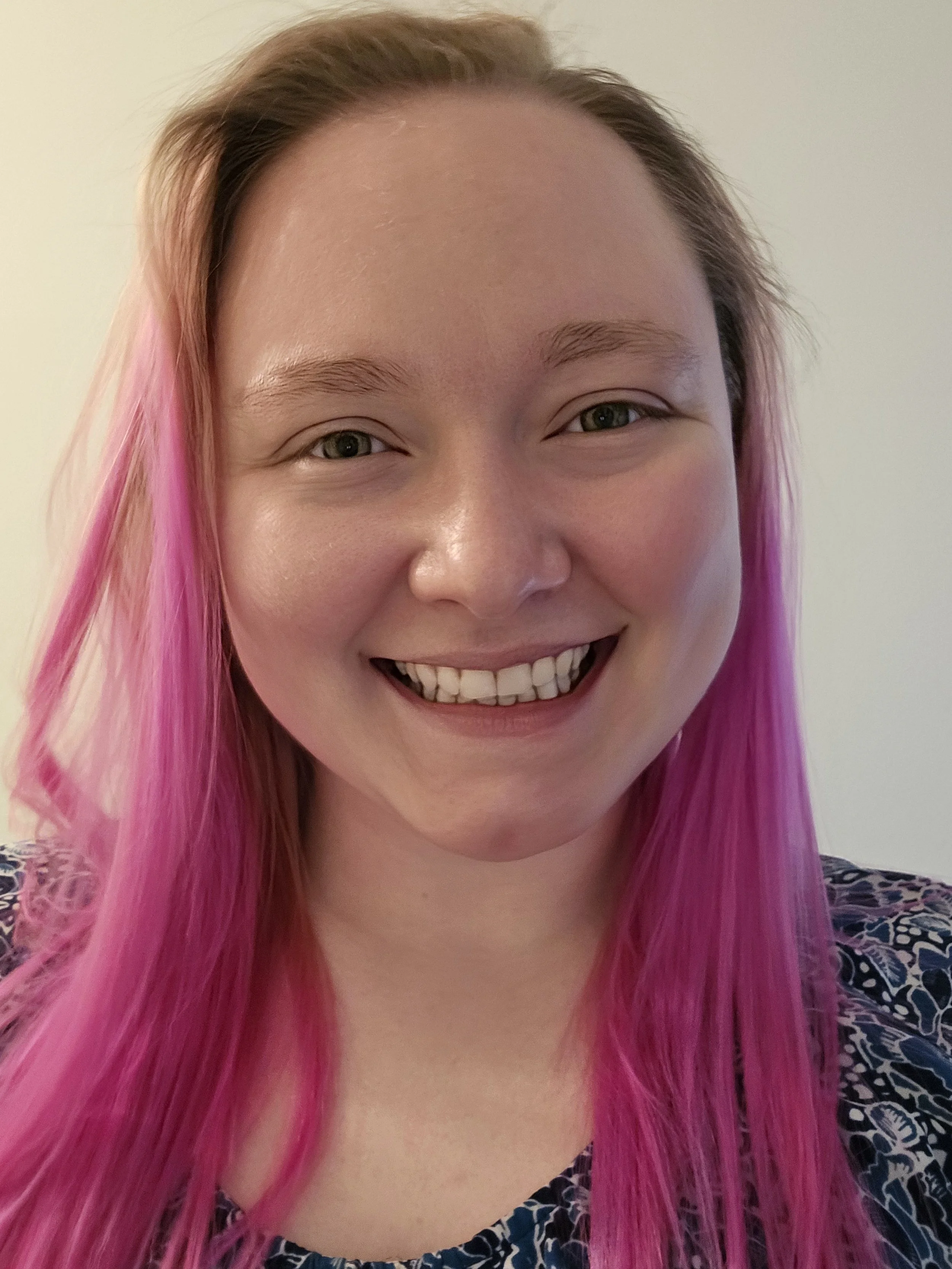 Chloe Koshiol-Wright, a pink haired fem presenting person wearing a blue flowered shirt.