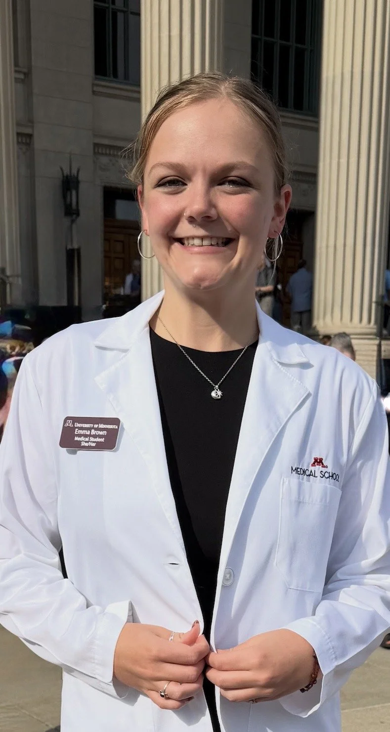 Emma Brown, a blonde woman, standing in a University of Minnesota Medical Student White Coat