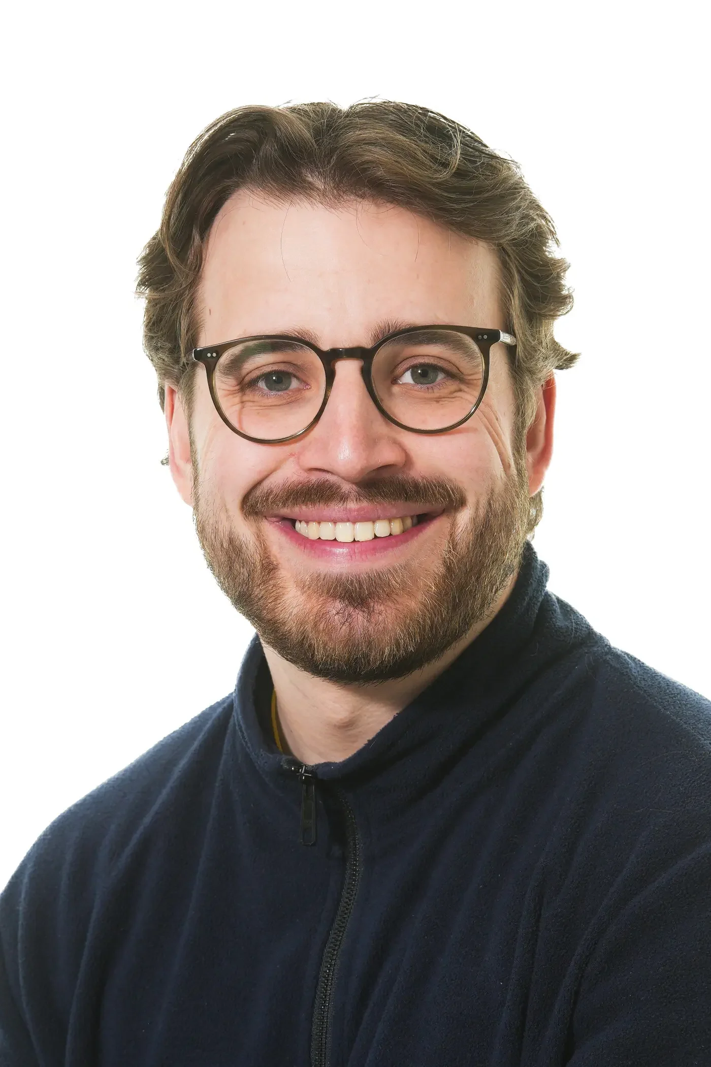 Et nærbillede af en glad mand med brunt, skæg og briller iført en sort hoodie.