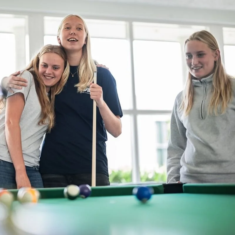Tre unge piger leger billiard i et lyst rum.