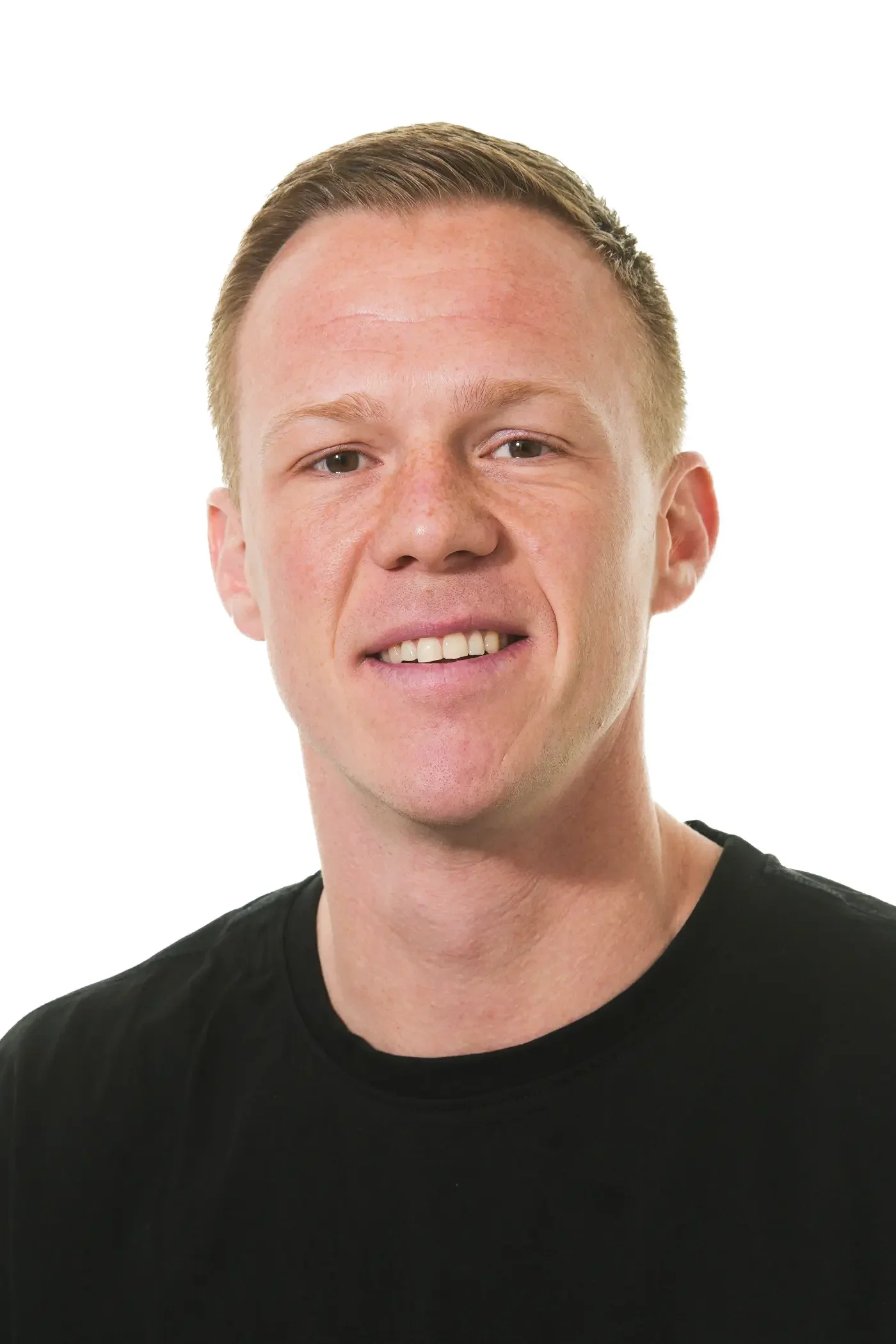 Billedet viser en mand med kort, rødt hår, smilende og iført en grå T-shirt, mod en hvid baggrund.