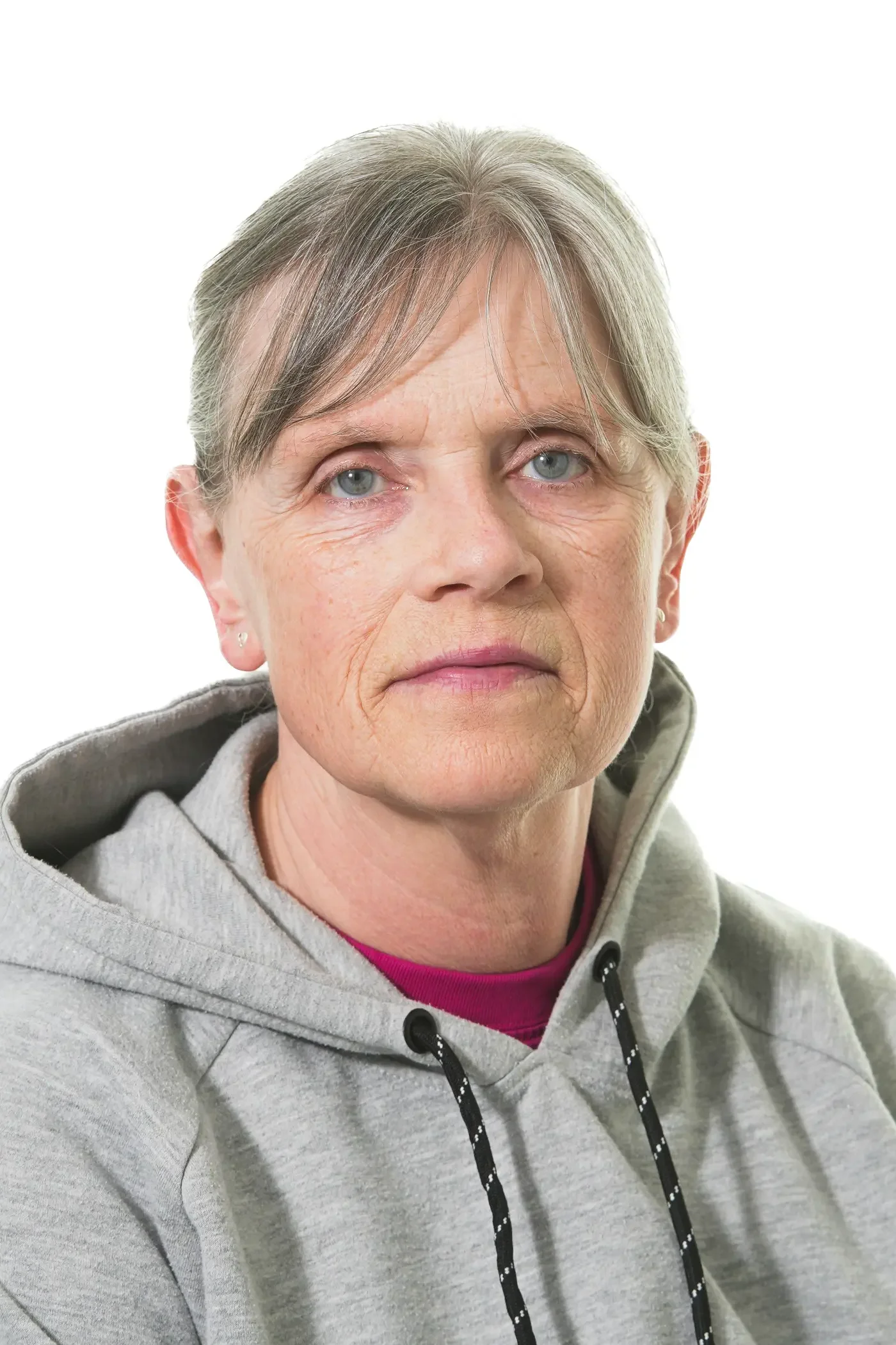 Et nærbillede af en ældre kvinde med gråt hår, blå øjne og et smil, iført en sort T-shirt mod en hvid baggrund.