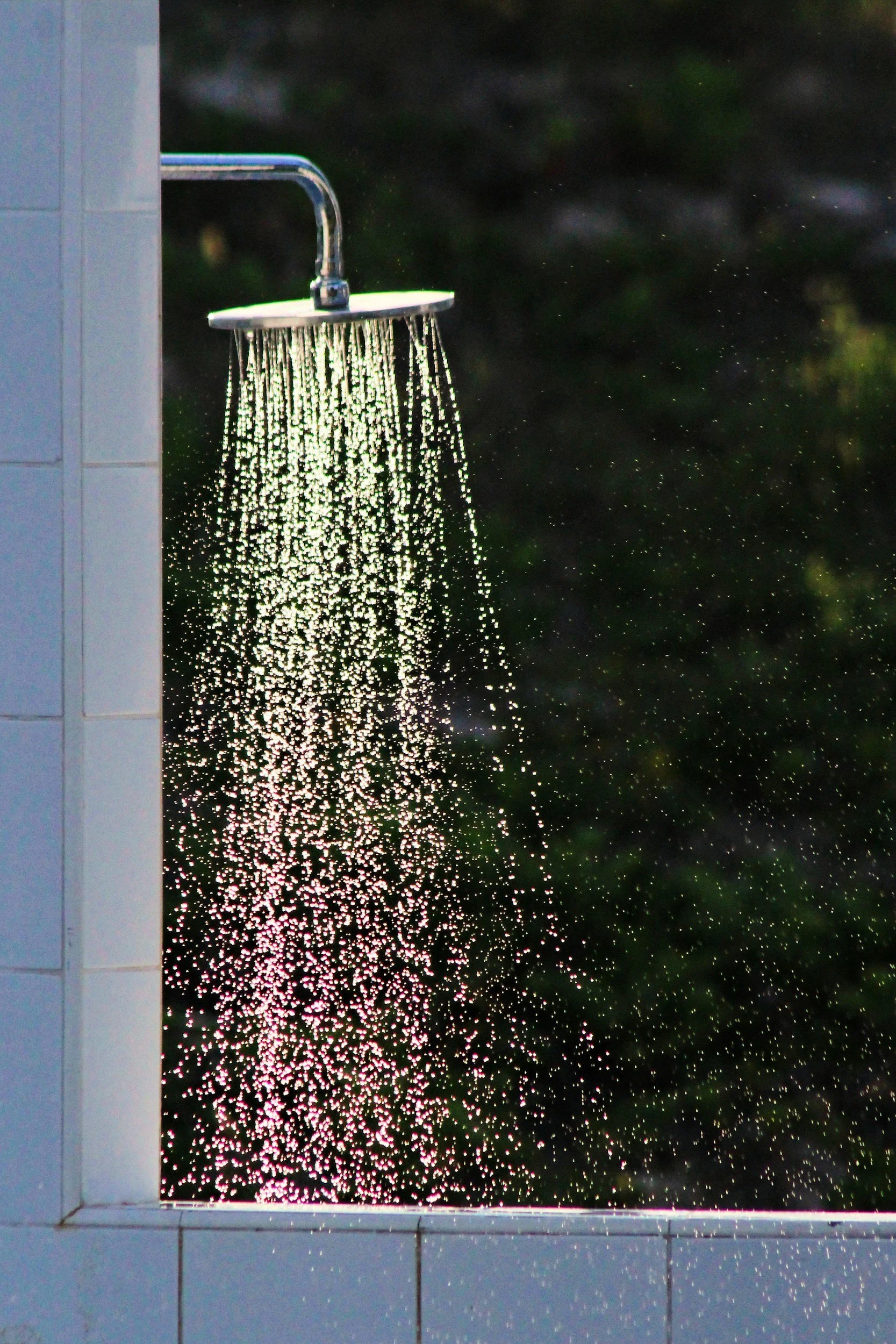 Outdoor shower with water running against a dark, leafy background.