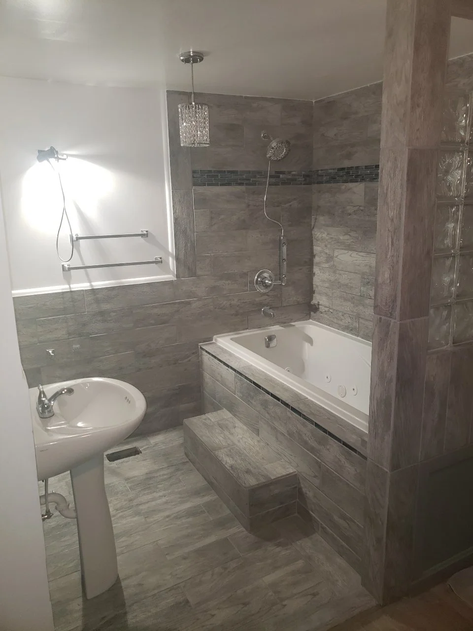 Bathroom with bathtub, walk-in shower, white sink, gray tiled walls and floor, and glass block wall