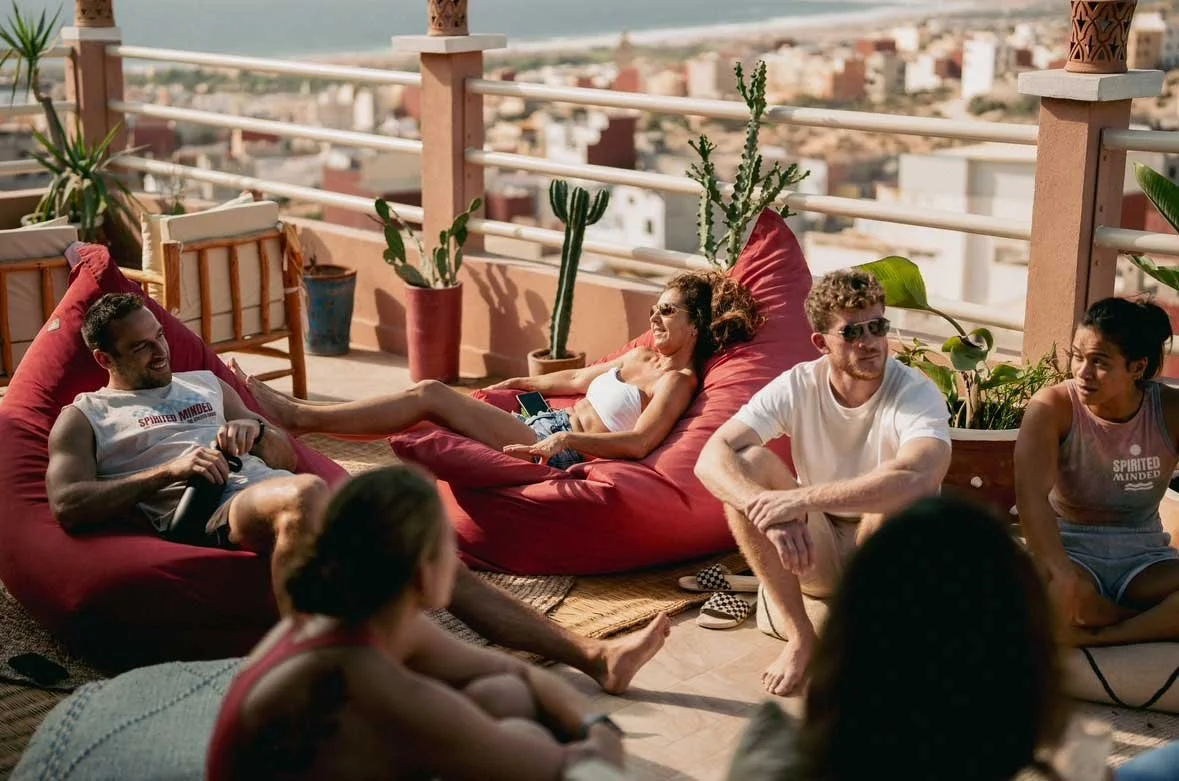 Group of friends relaxing on a rooftop balcony with potted plants and city view in the background.