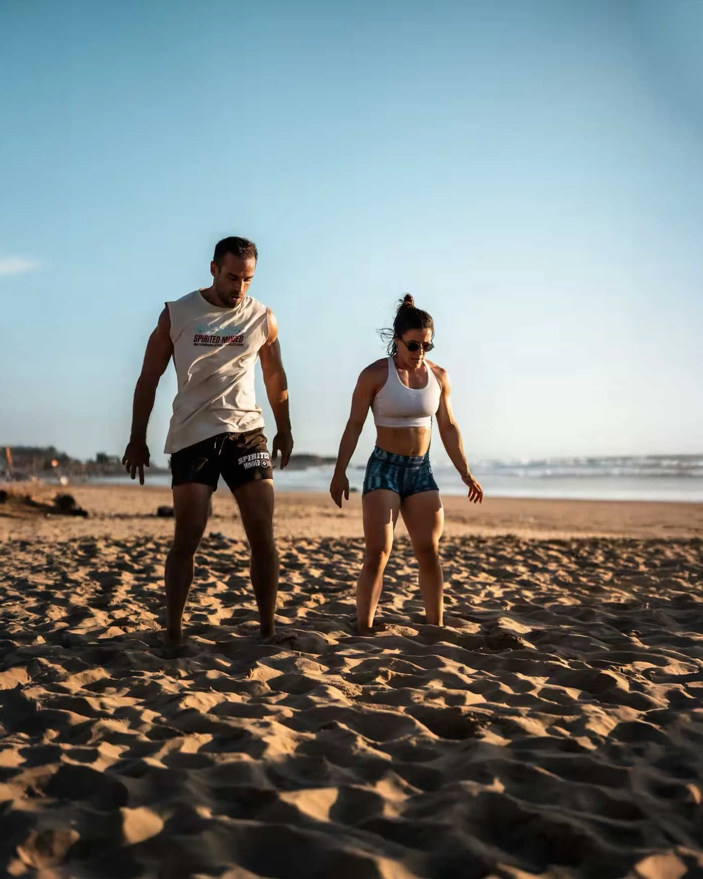 A man and woman walking on a sandy beach during sunset