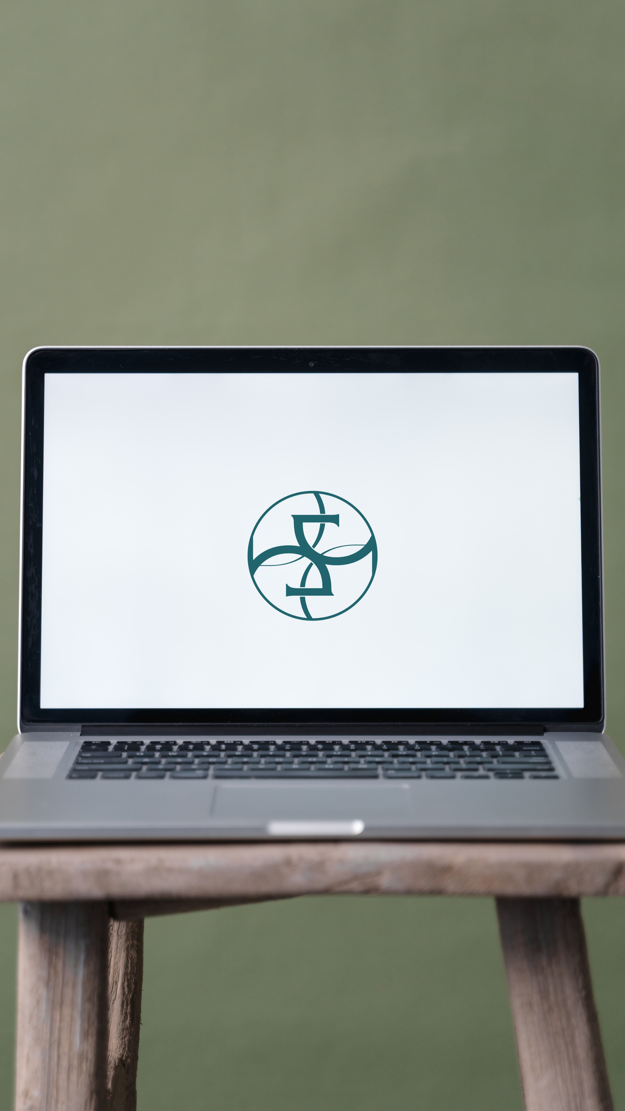 A laptop on a wooden table displaying a circular logo with stylized letters on a white background.