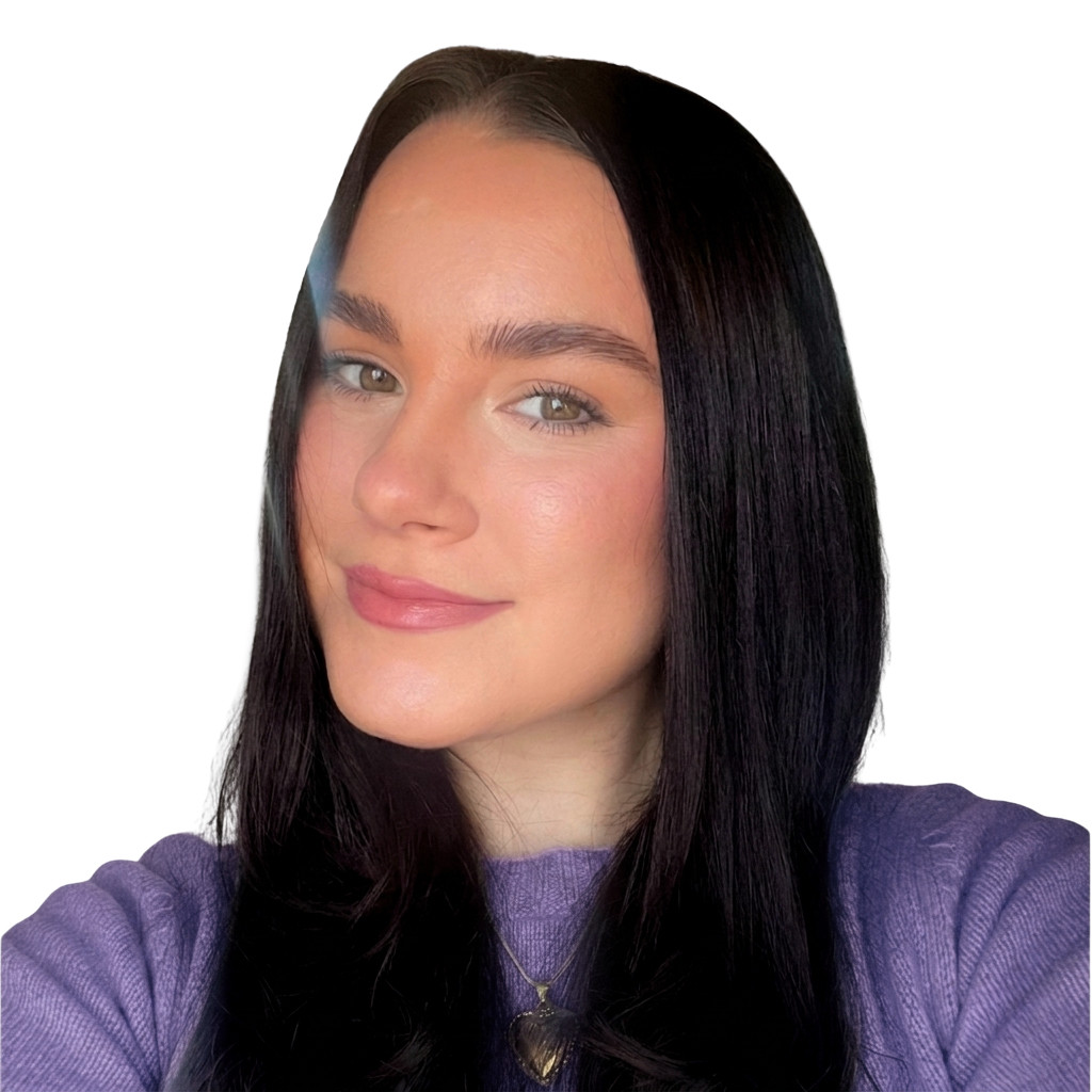 A woman with long dark hair, hazel eyes, and a light complexion, wearing a purple shirt and a heart-shaped necklace, smiling softly against a white background.