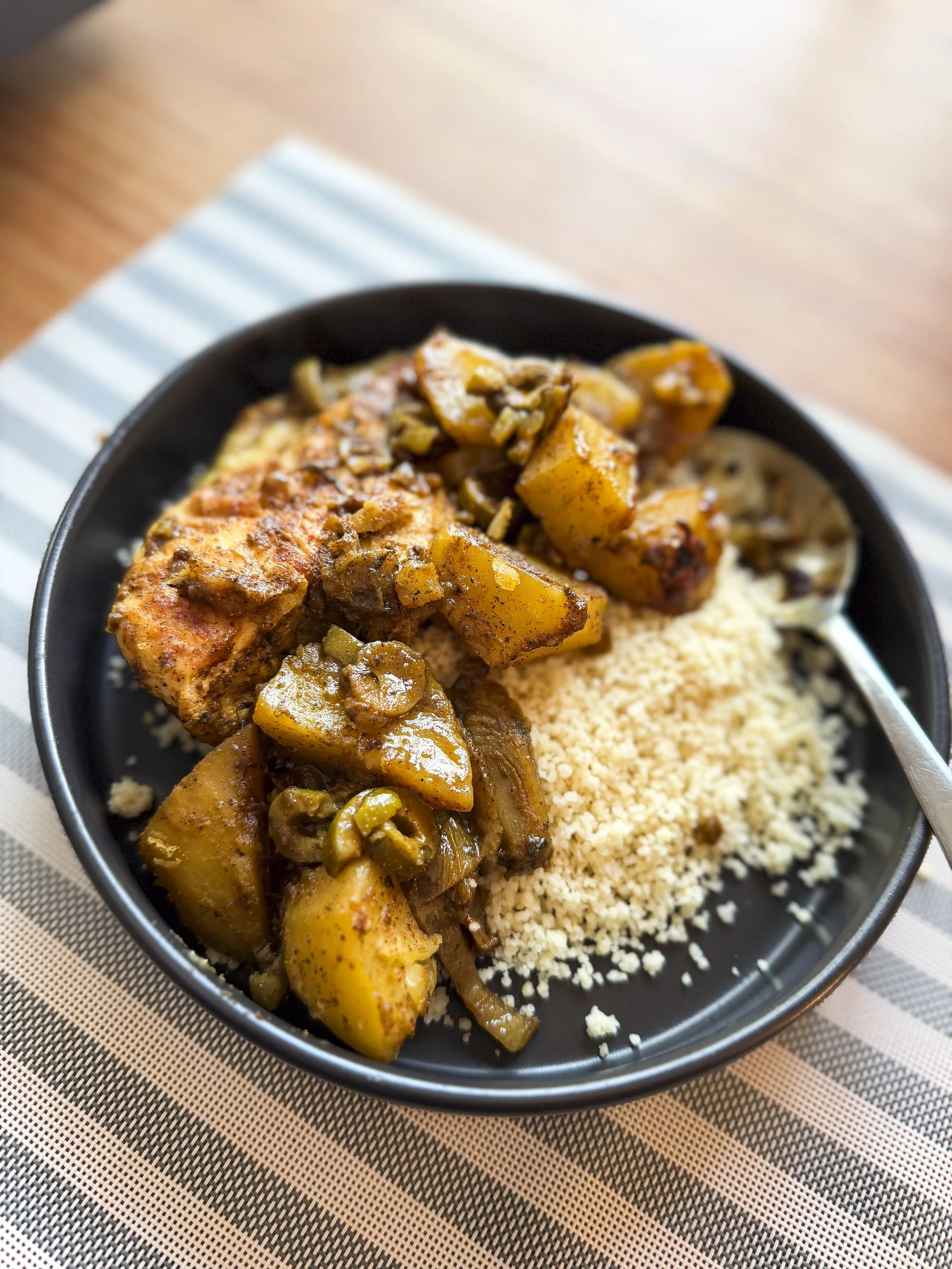 Chicken tagine with potatoes and green olives served in a black bowl with couscous