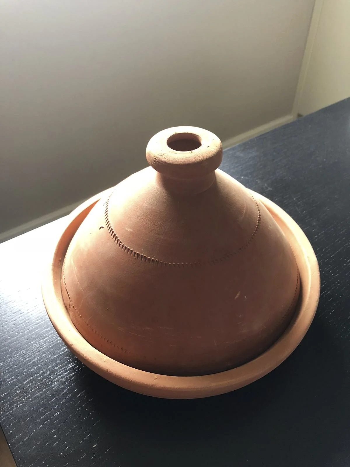 Traditional Moroccan clay tagine pot on a dark surface, brought back from Morocco