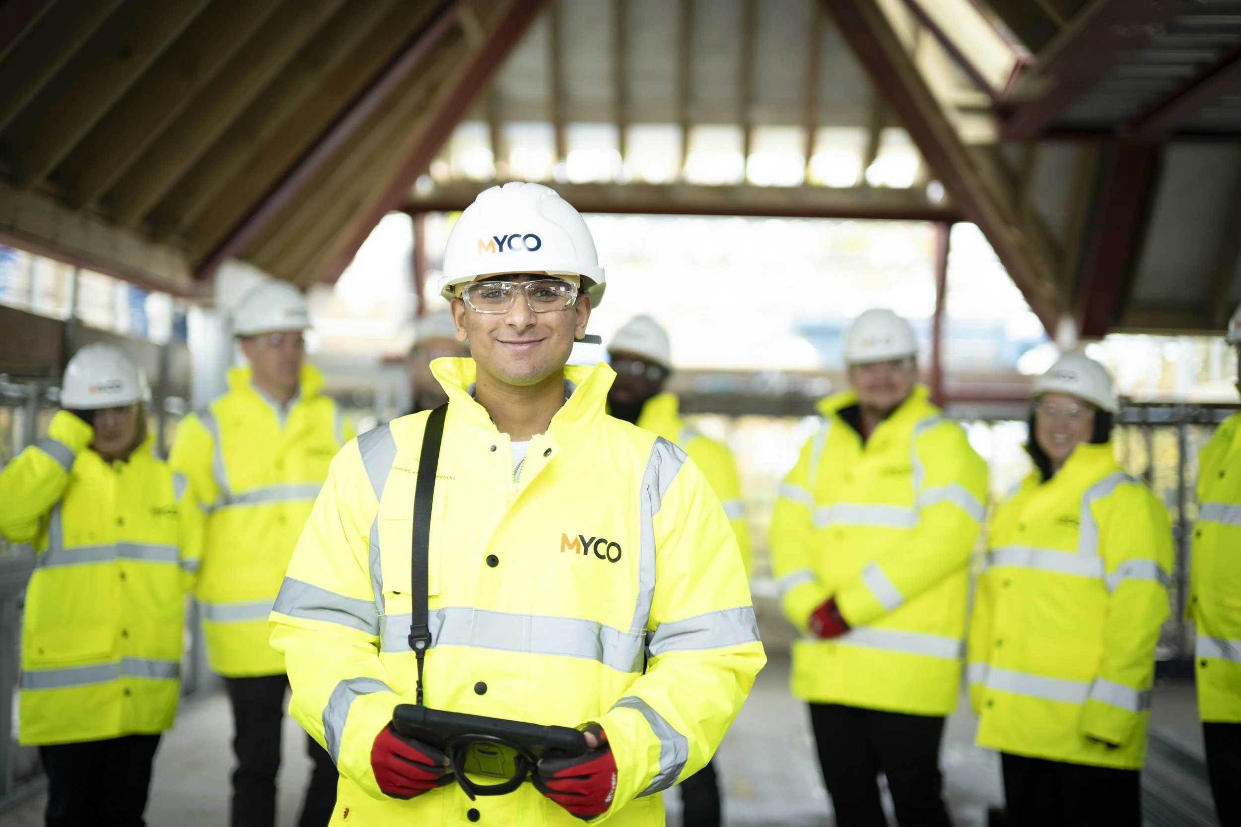 Group of construction workers on scaffolding at a construction site, wearing helmets and safety vests, with the MYCO logo in the top right corner and the phrase 'Future Driven Construction' at the bottom.