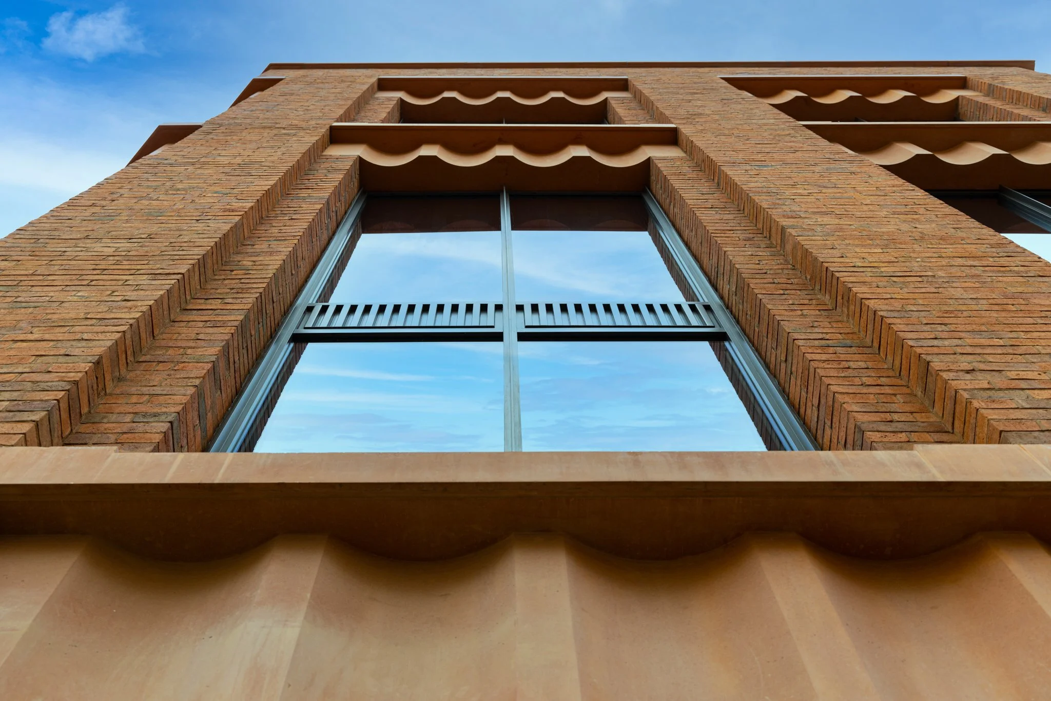 Low-angle view of a brick building with a large glass window and decorative brown awnings against a blue sky.