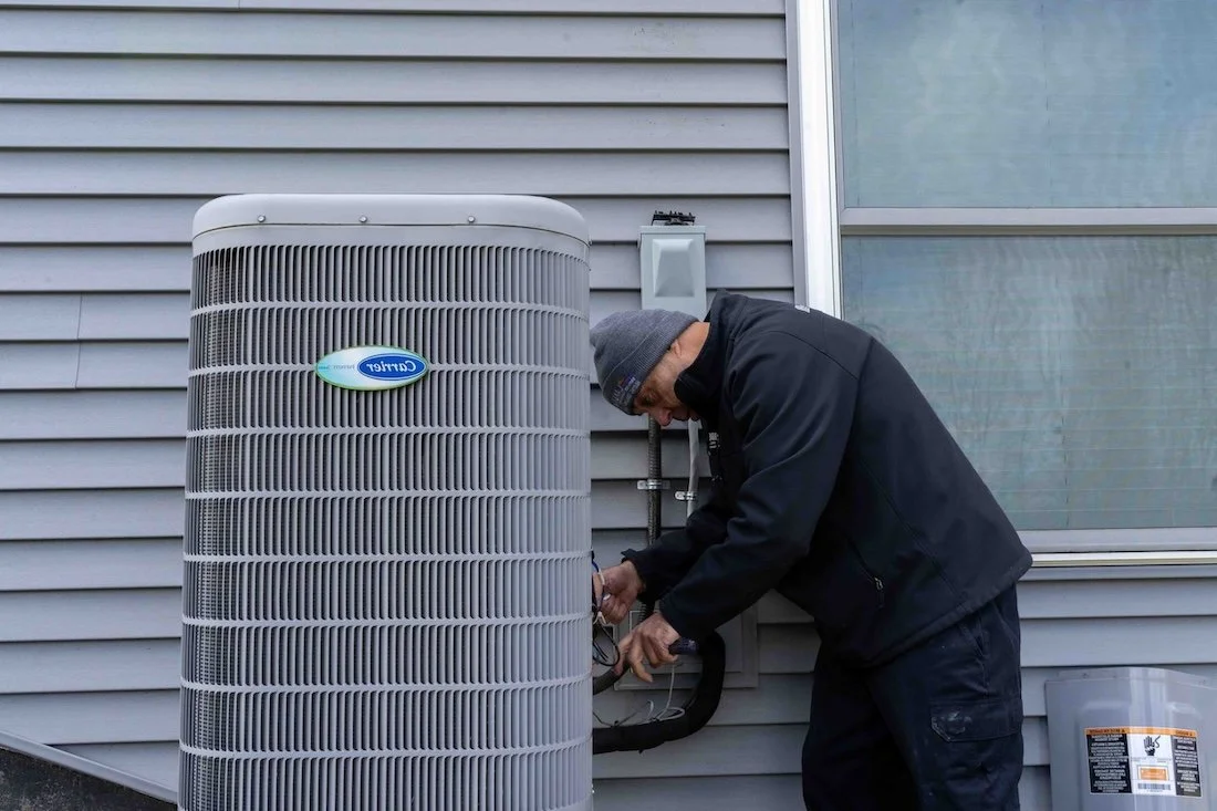 A technician working on an outdoor air conditioning unit near a house wall.