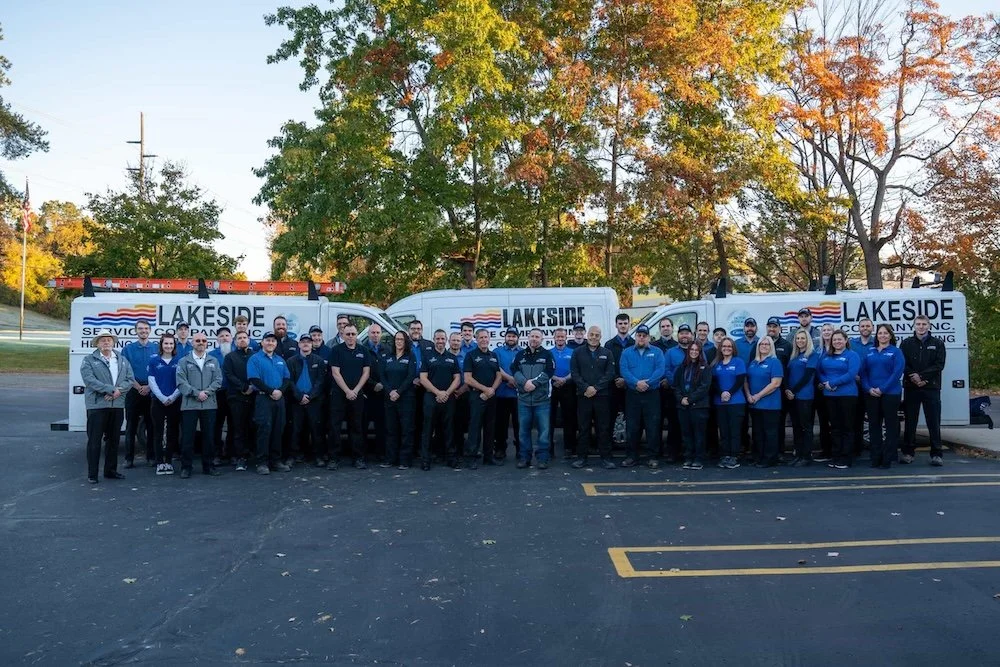 Group of service technicians and staff members standing in front of service trucks with 'Lakeside' branding in a parking lot during autumn.