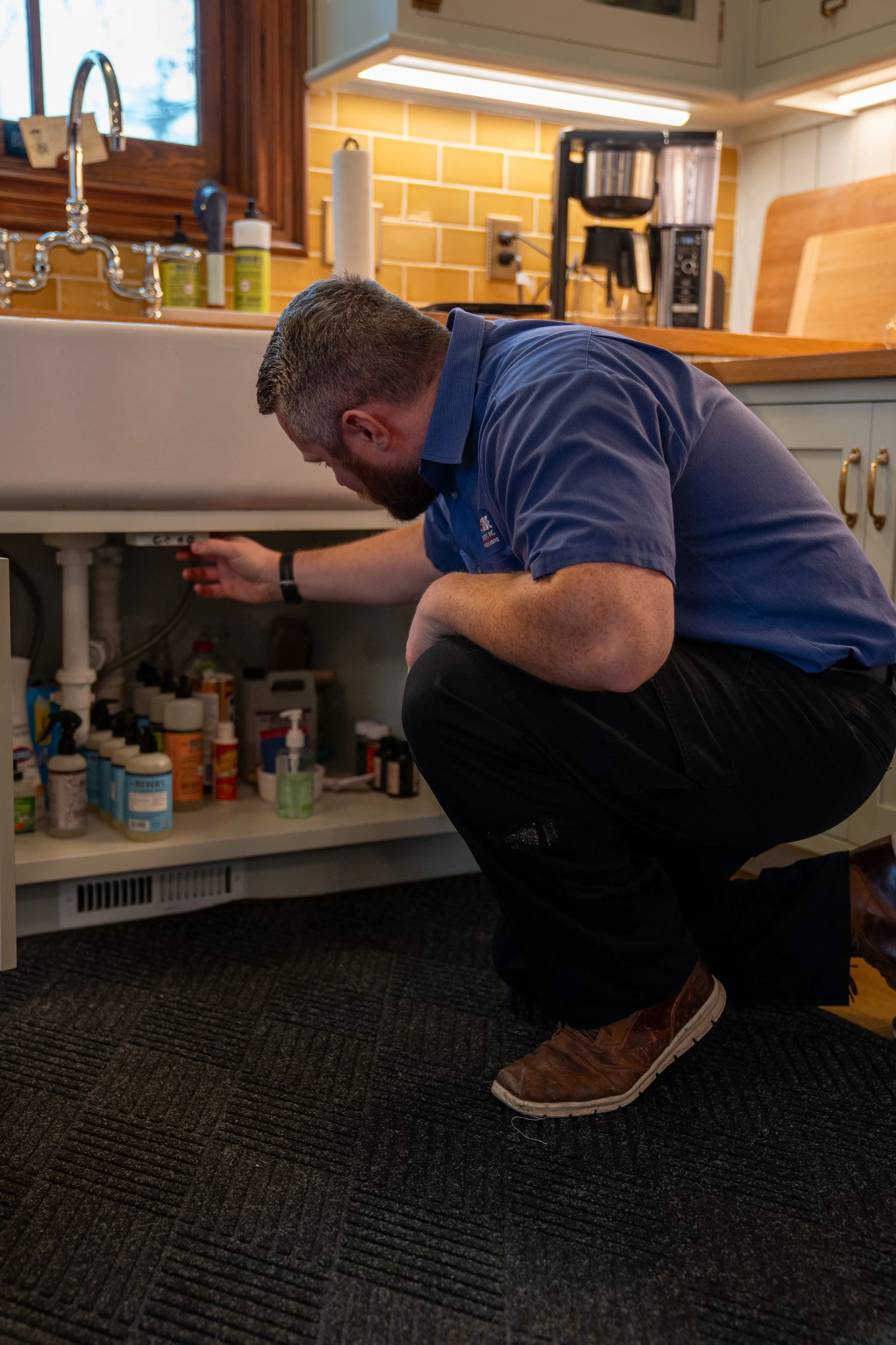 Lakeside plumber inspecting under-sink plumbing and water lines in a Michigan home