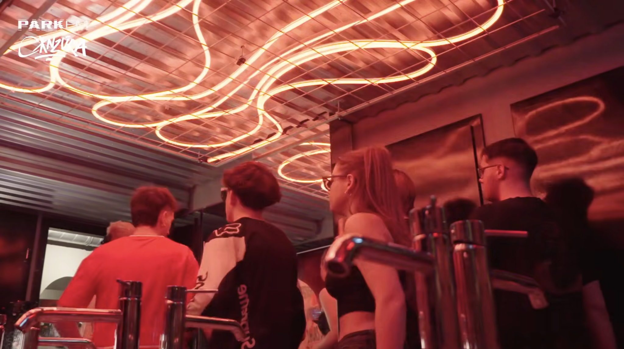 People sitting at a bar or restaurant with red neon light fixtures on the ceiling and a dark reflective wall behind them.