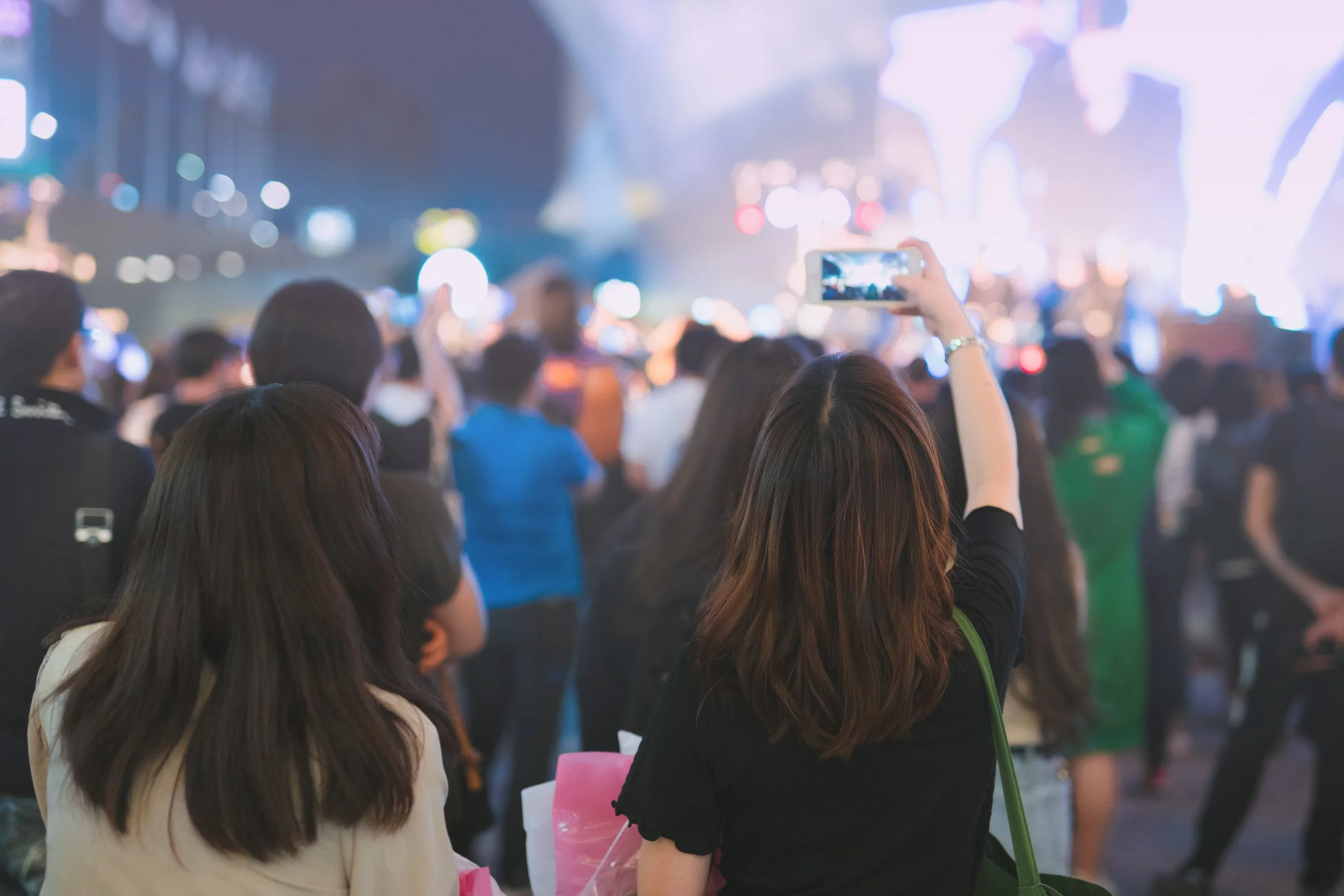 Crowd at a concert with a person taking a photo on a smartphone.