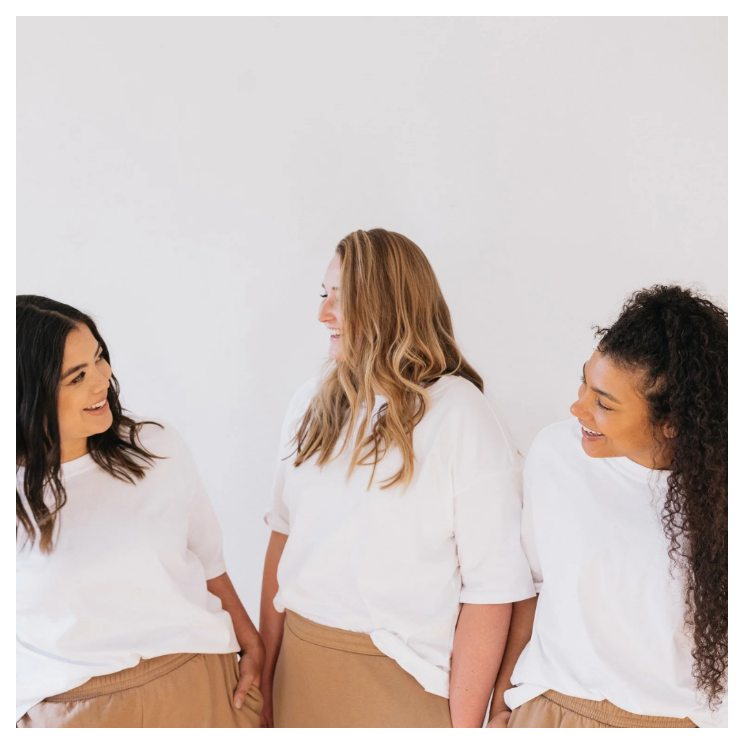 Three women smiling and talking together in a bright wellness setting.