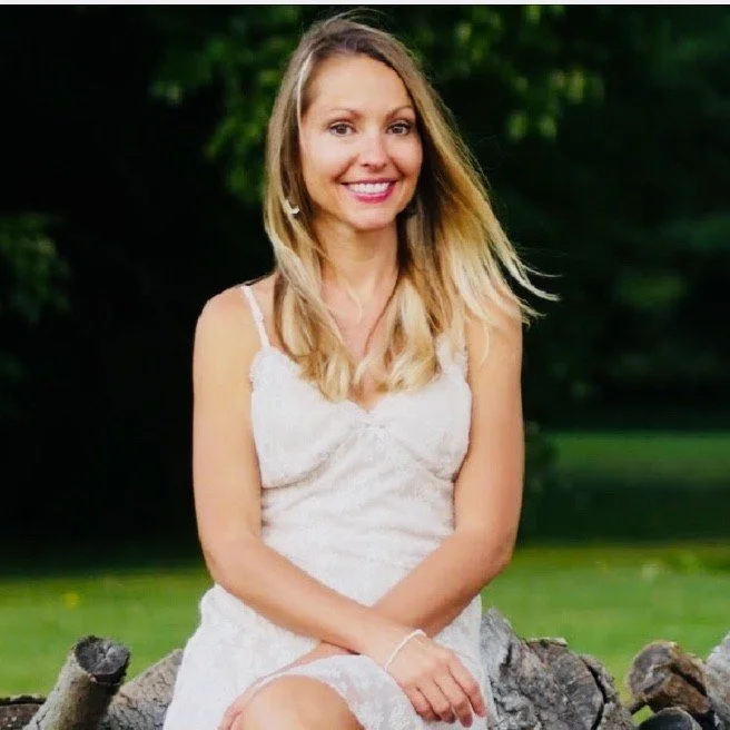 Karen Burr, a clinical herbalist,  sitting in nature in a white dress smiling