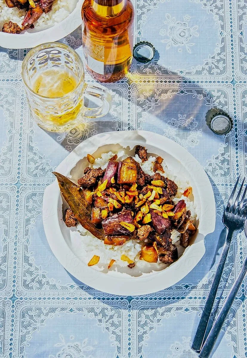 Plate of beef stir-fry with vegetables and rice on a lace tablecloth, a bottle of beer, a glass of beer, and some bottle caps.