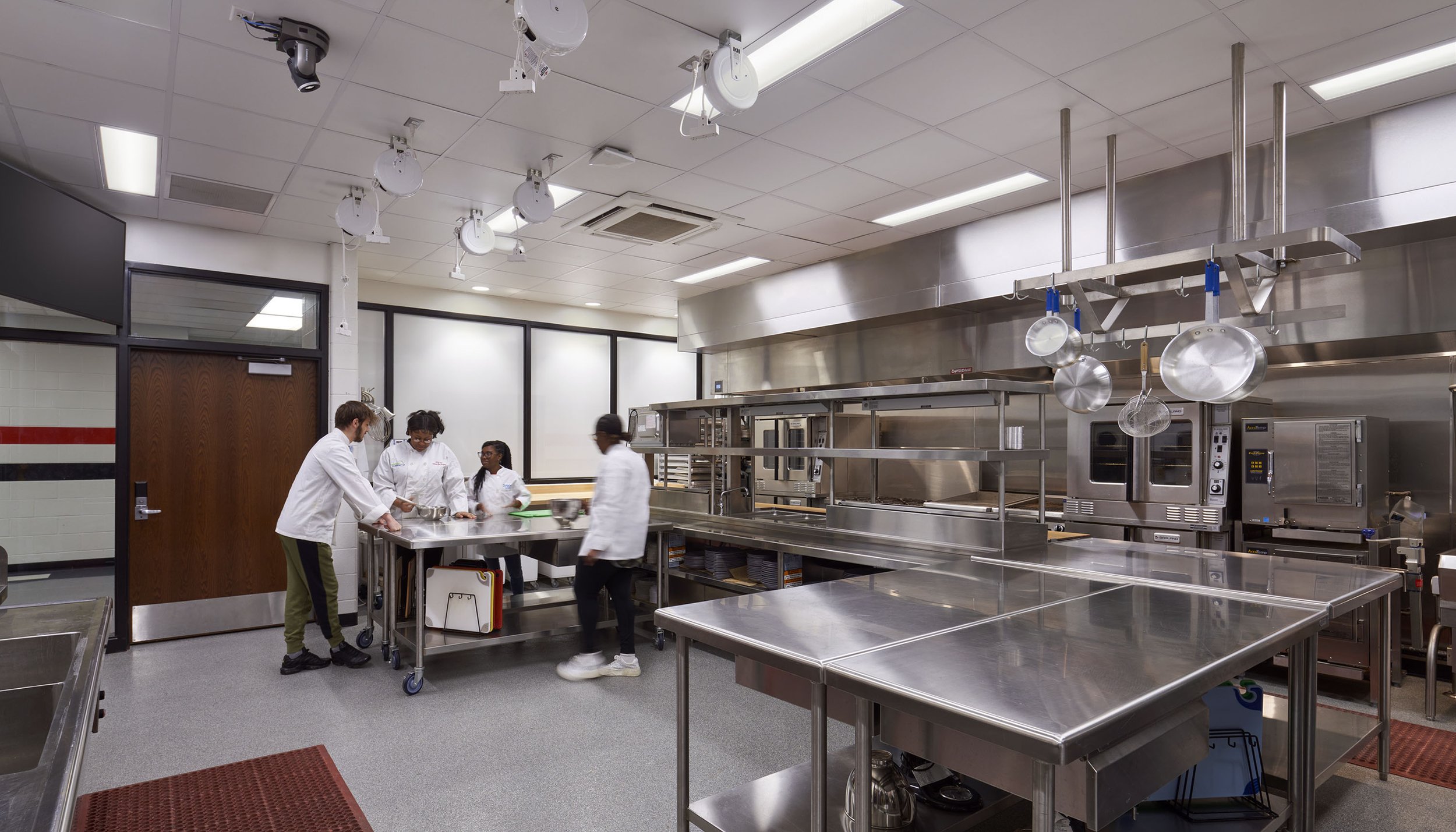 In the commercial-grade culinary lab, an adjoining interactive classroom allows for a separate instruction area. The overall goal was to create cohesive "one school" identity at both campuses. Red, black, and gray accents show off the new school colo