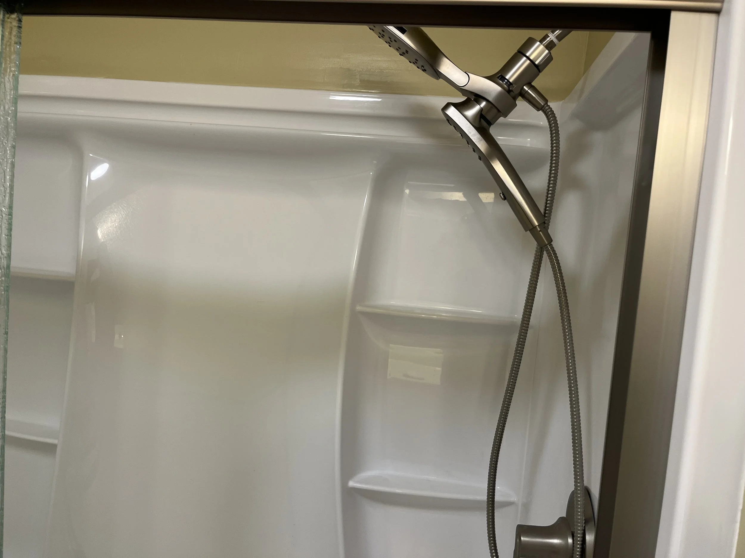 Inside a white shower with a handheld showerhead attached to a flexible hose, mounted at an angle on the wall.