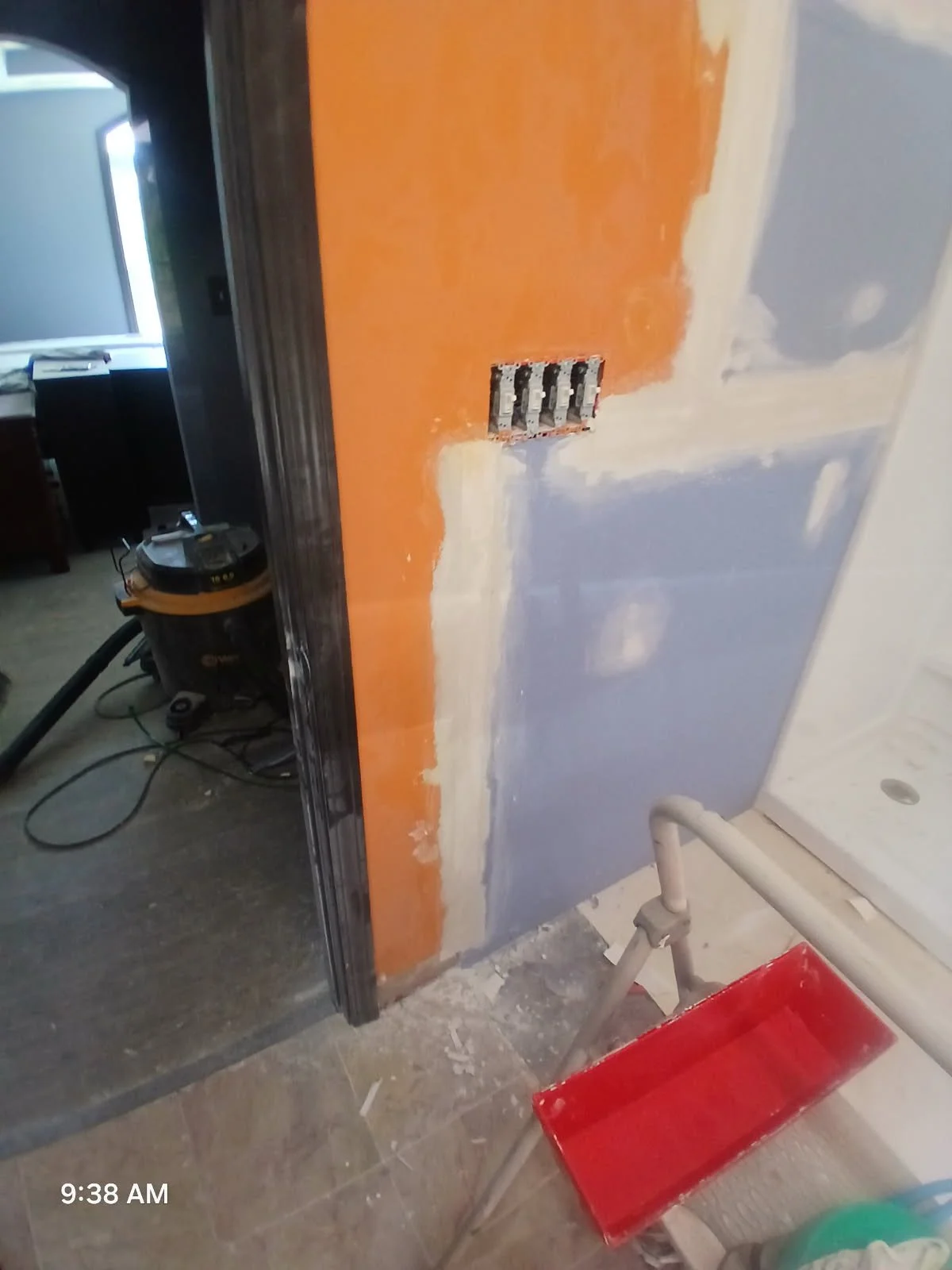 Partial view of a room under renovation showing a wall with multiple colors, an electrical outlet box without cover, and construction tools on the floor.