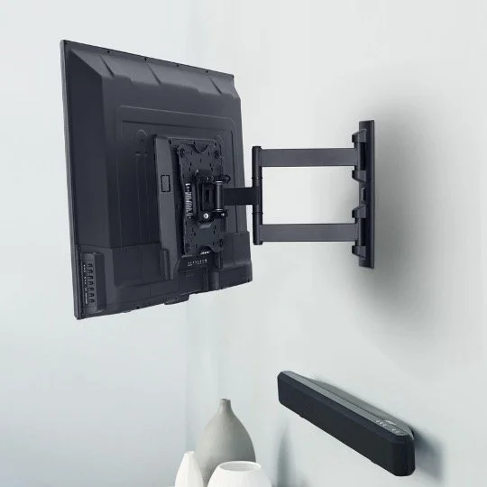Wall-mounted monitor with adjustable arm, a soundbar beneath it, and a white vase on a shelf.