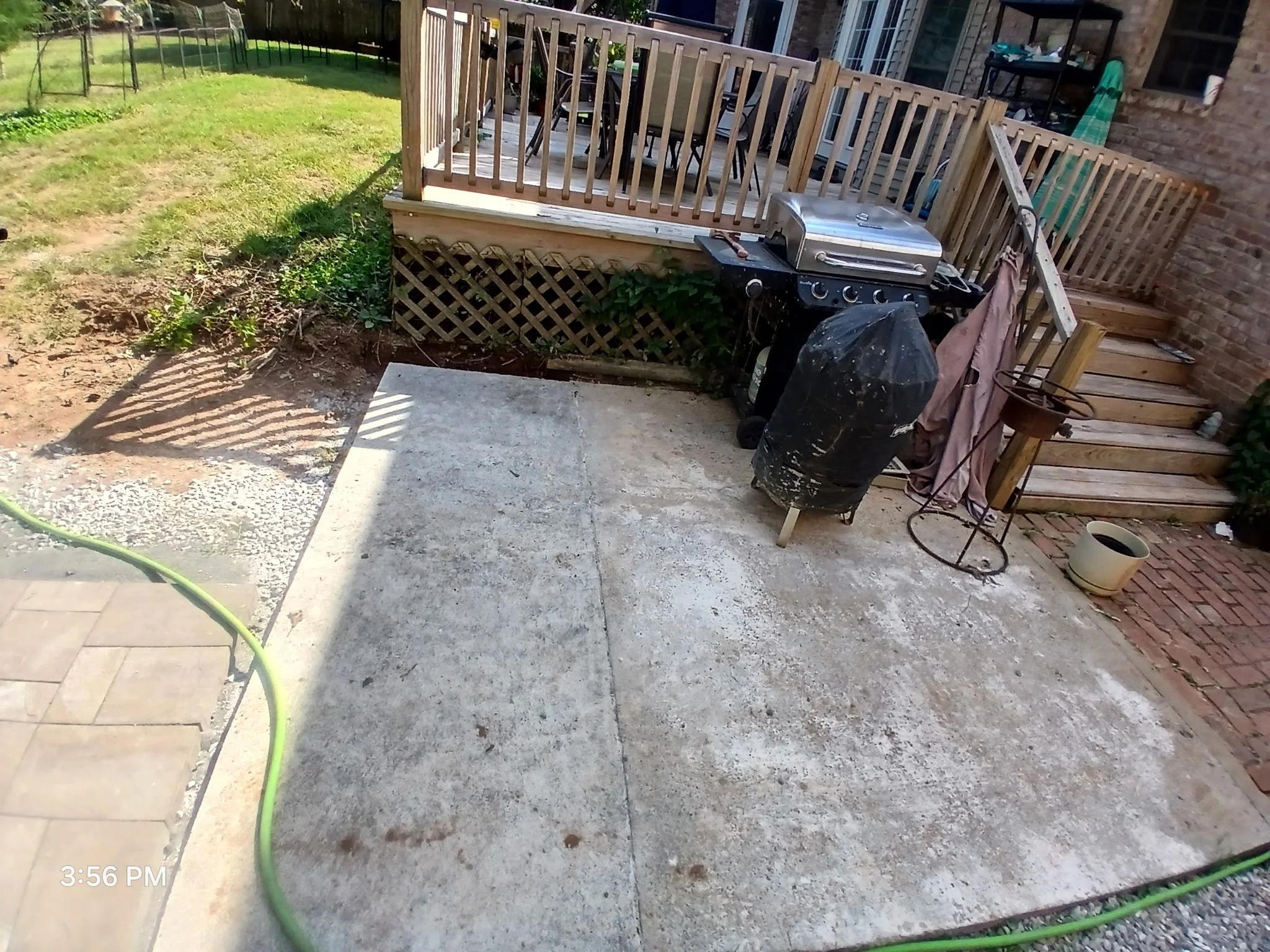 Backyard patio area with a newly poured concrete slab, a black grill covered with a black tarp, a foldable chair, and a set of wooden stairs leading to a screened porch.