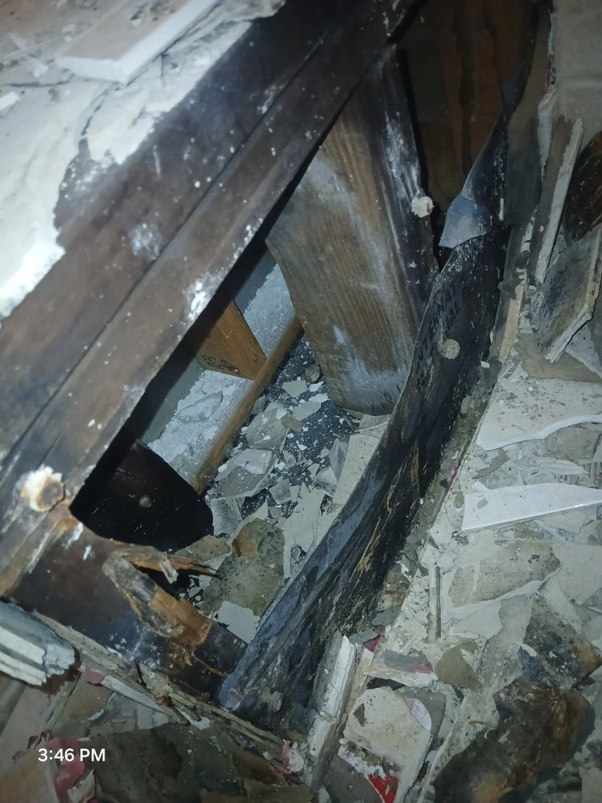 A hole in a wooden floor with debris and broken tiles around it.