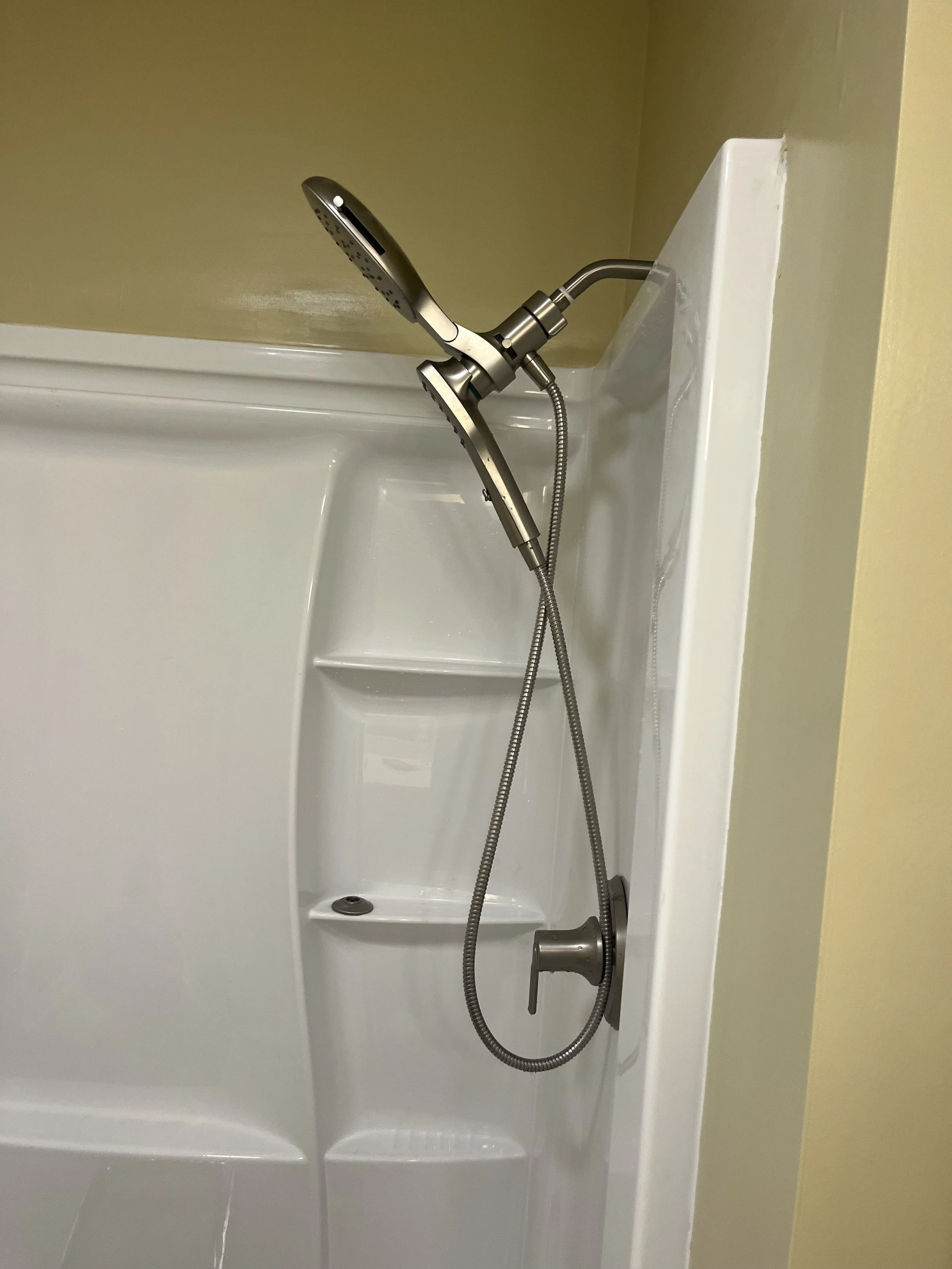 Shower with handheld showerhead mounted on a wall inside a white acrylic shower stall.