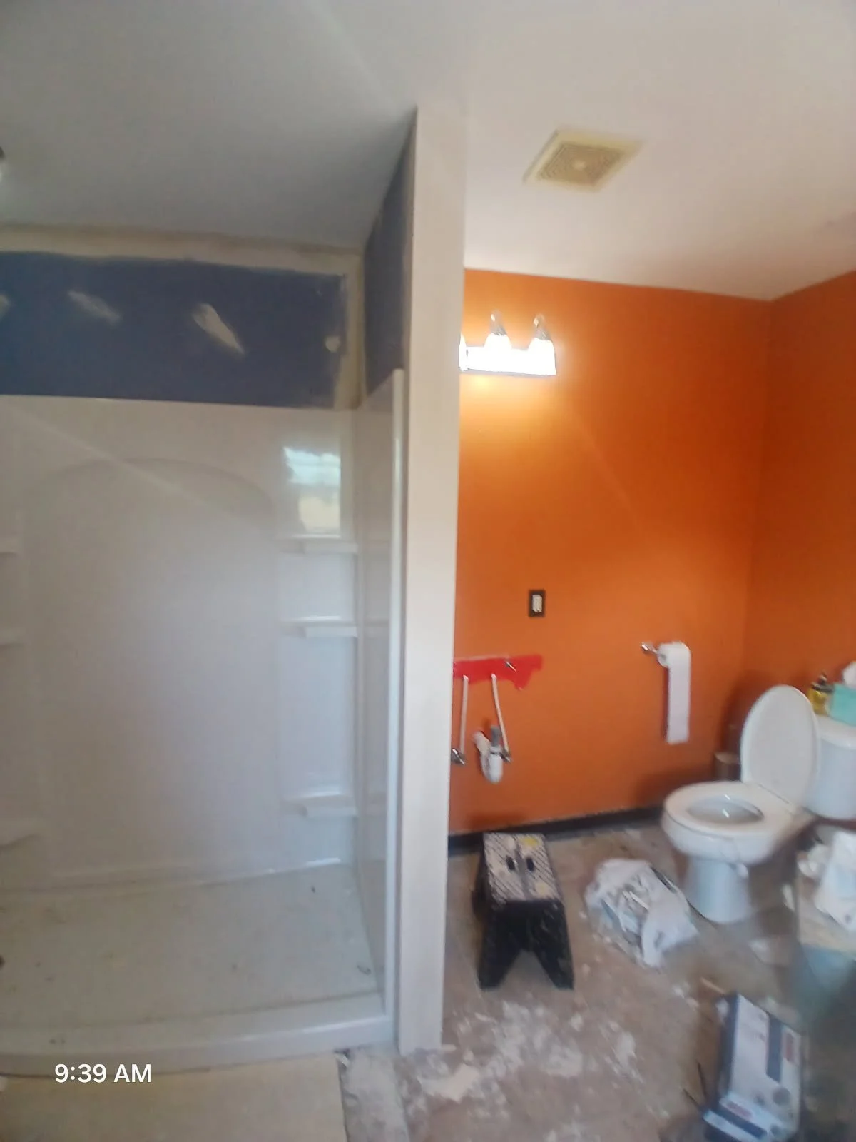 Bathroom under renovation with orange wall, toilet, rail, and shower stall on the left side.