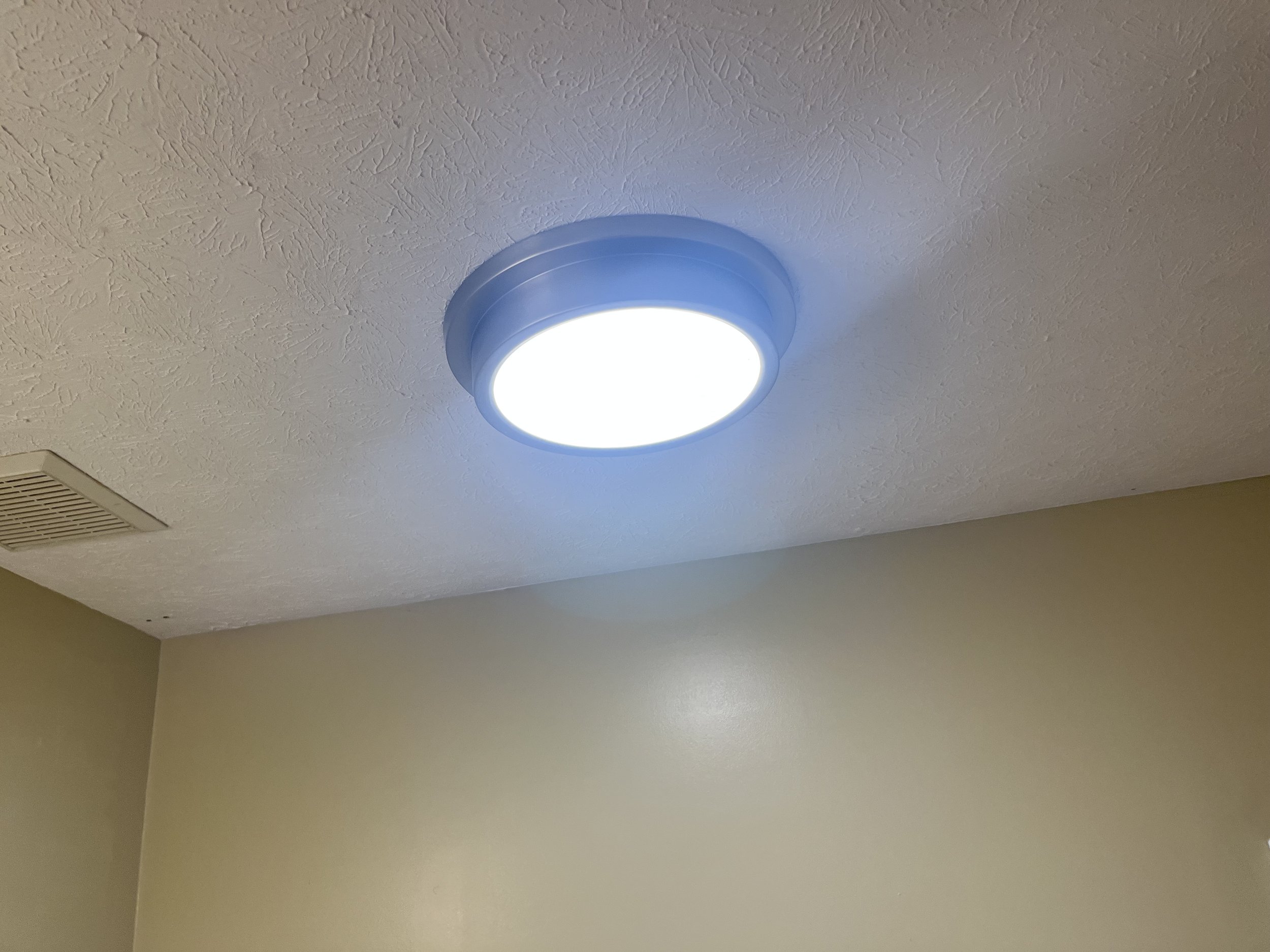Ceiling light fixture emitting bright white light in a room with beige walls and textured ceiling.