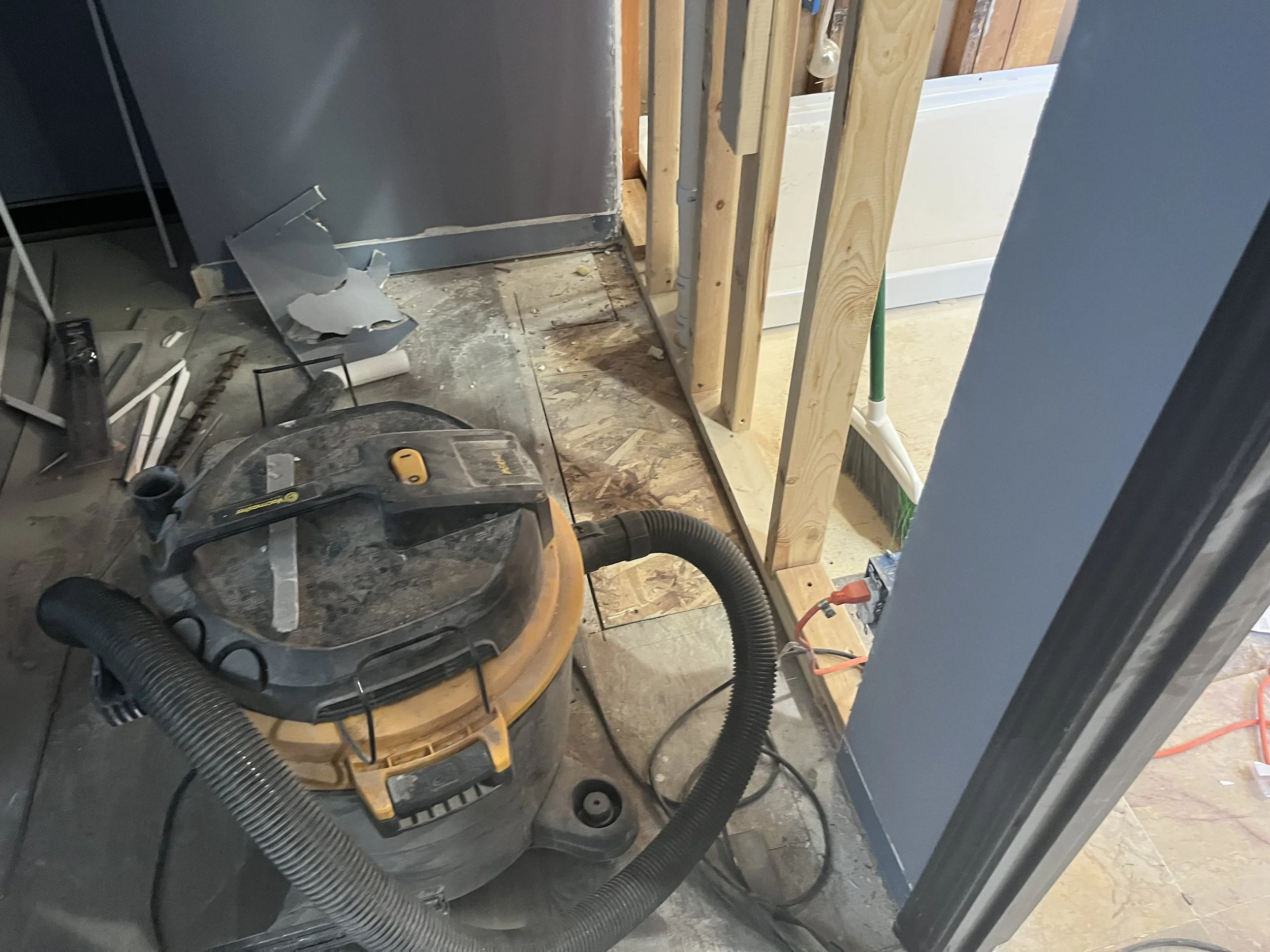 Construction site with a shop vacuum cleaner, debris, and exposed wooden framing.