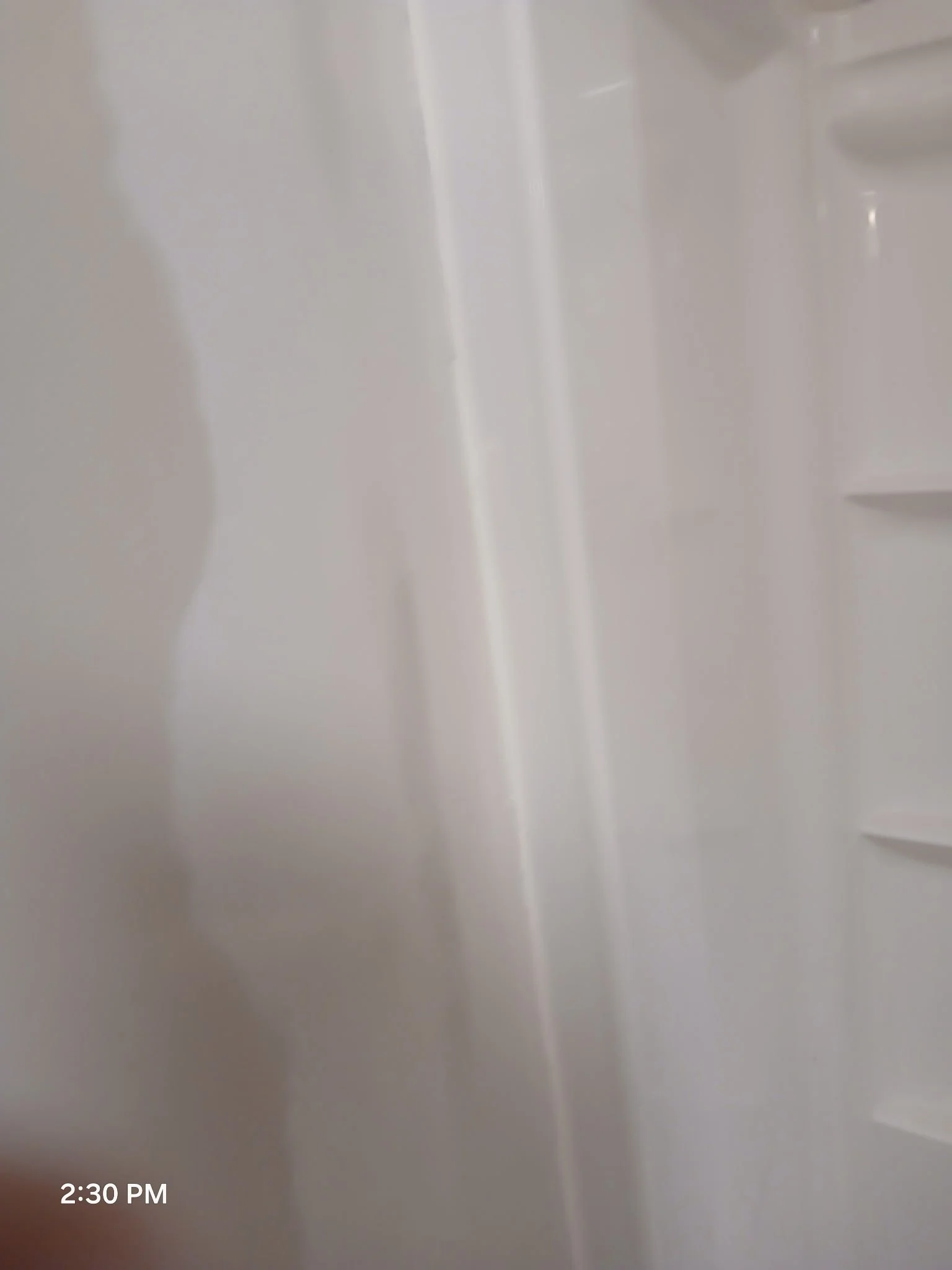 Close-up of a white shower or bathtub wall with built-in shelves and a shadow on the left side.