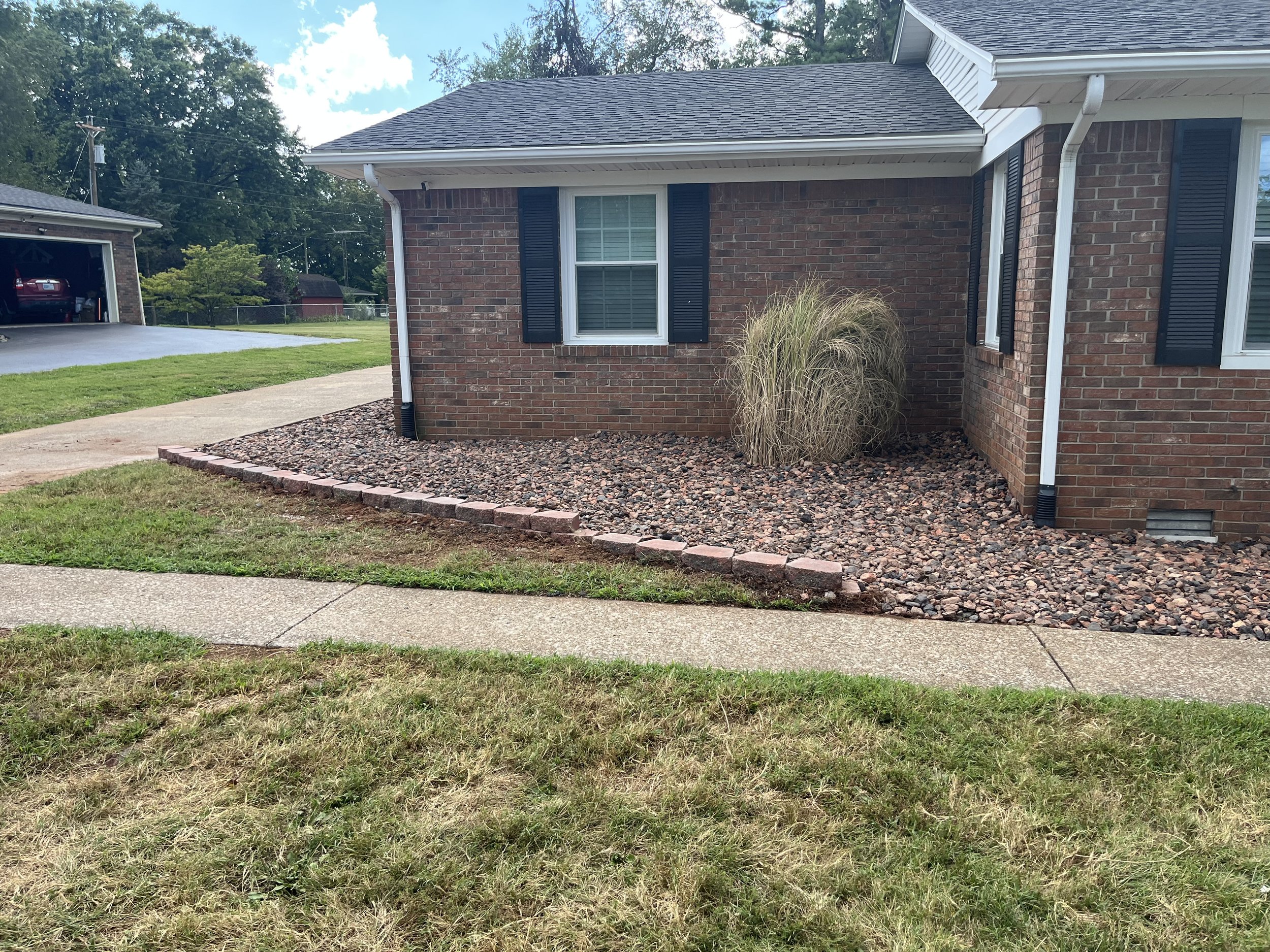 Front yard with a brick house, a sidewalk, and a rock bed with one bush